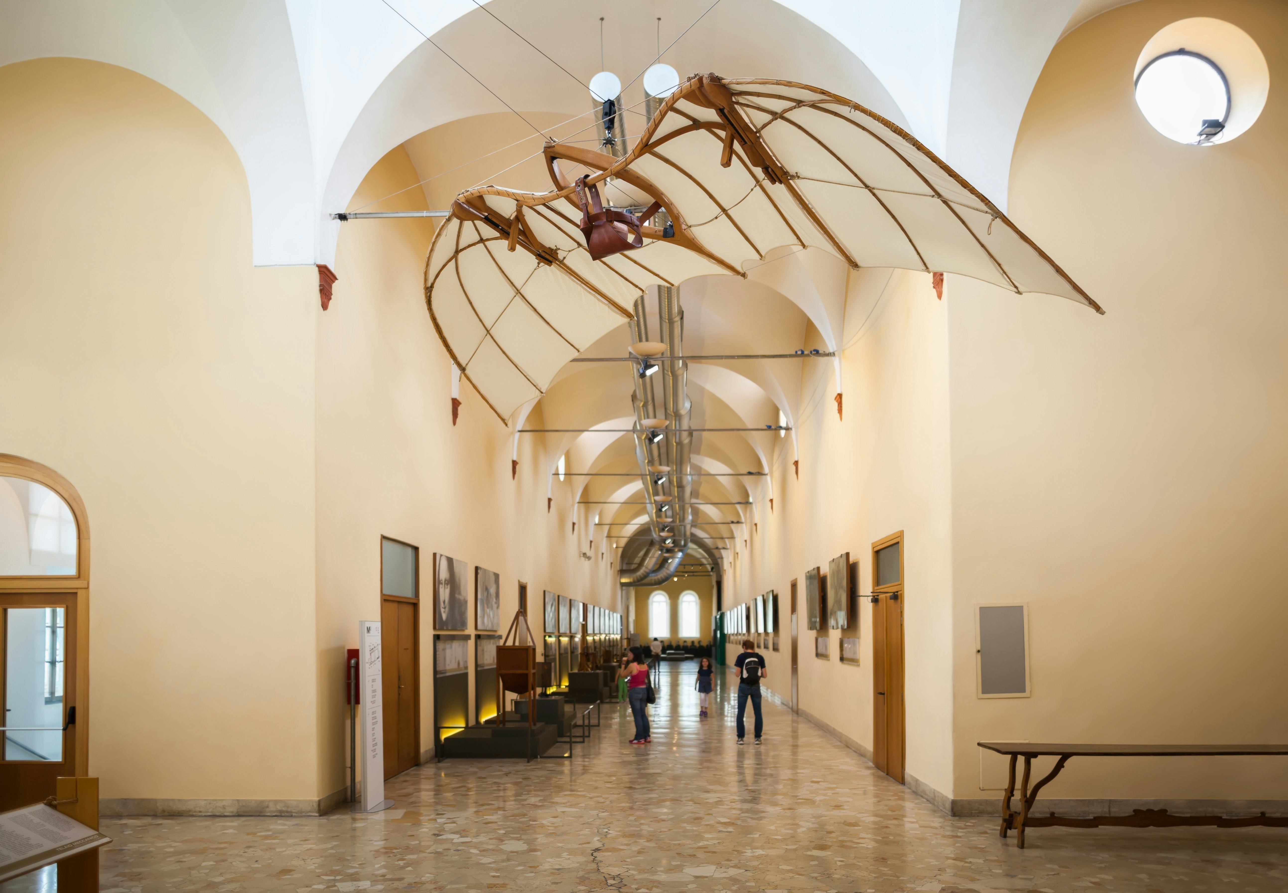 A corridor in a museum with displays on the walls. Above hangs a paraglider-like structure.