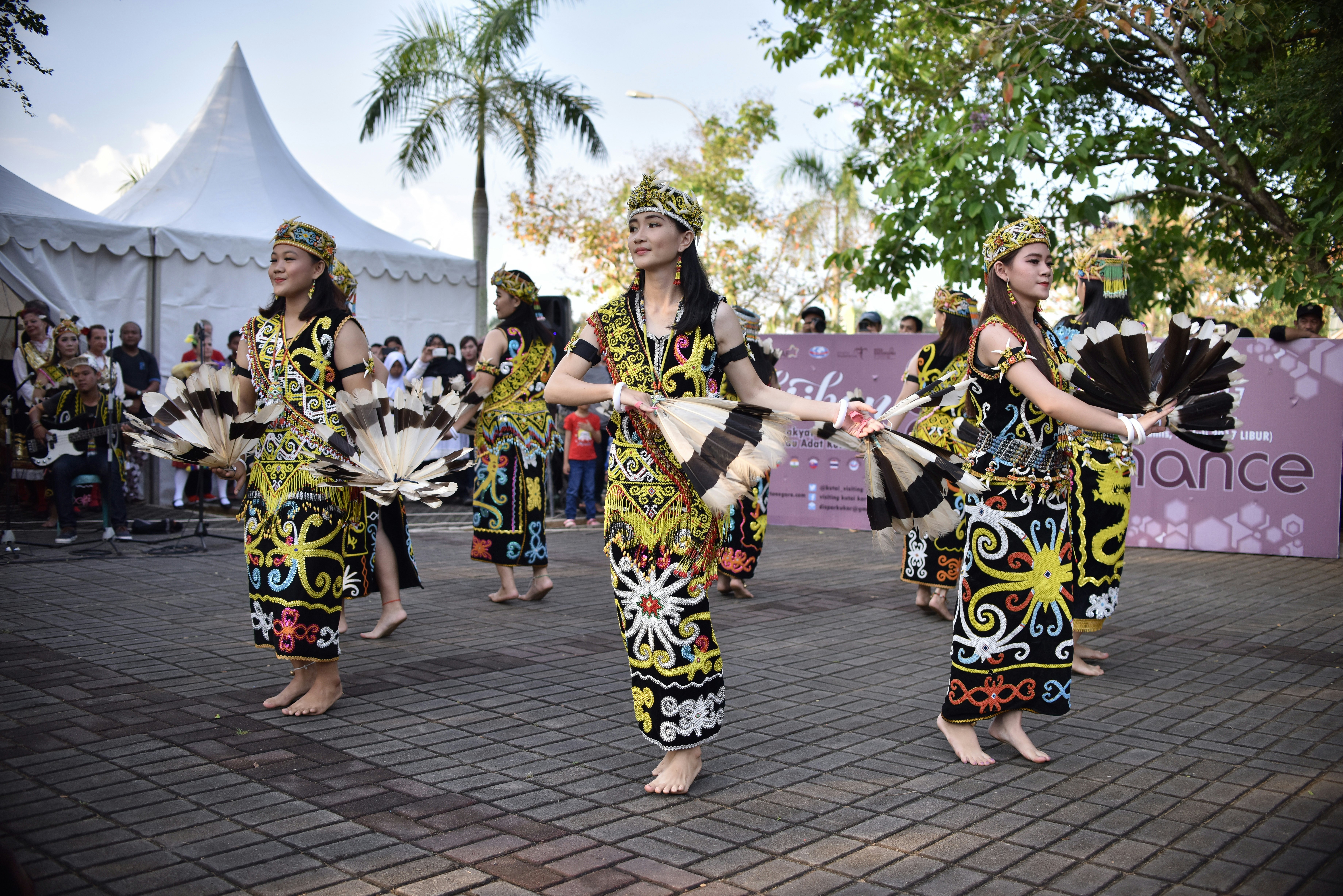 Women in brightly printed dresses wave fans as part of a dance performance at a public festival.