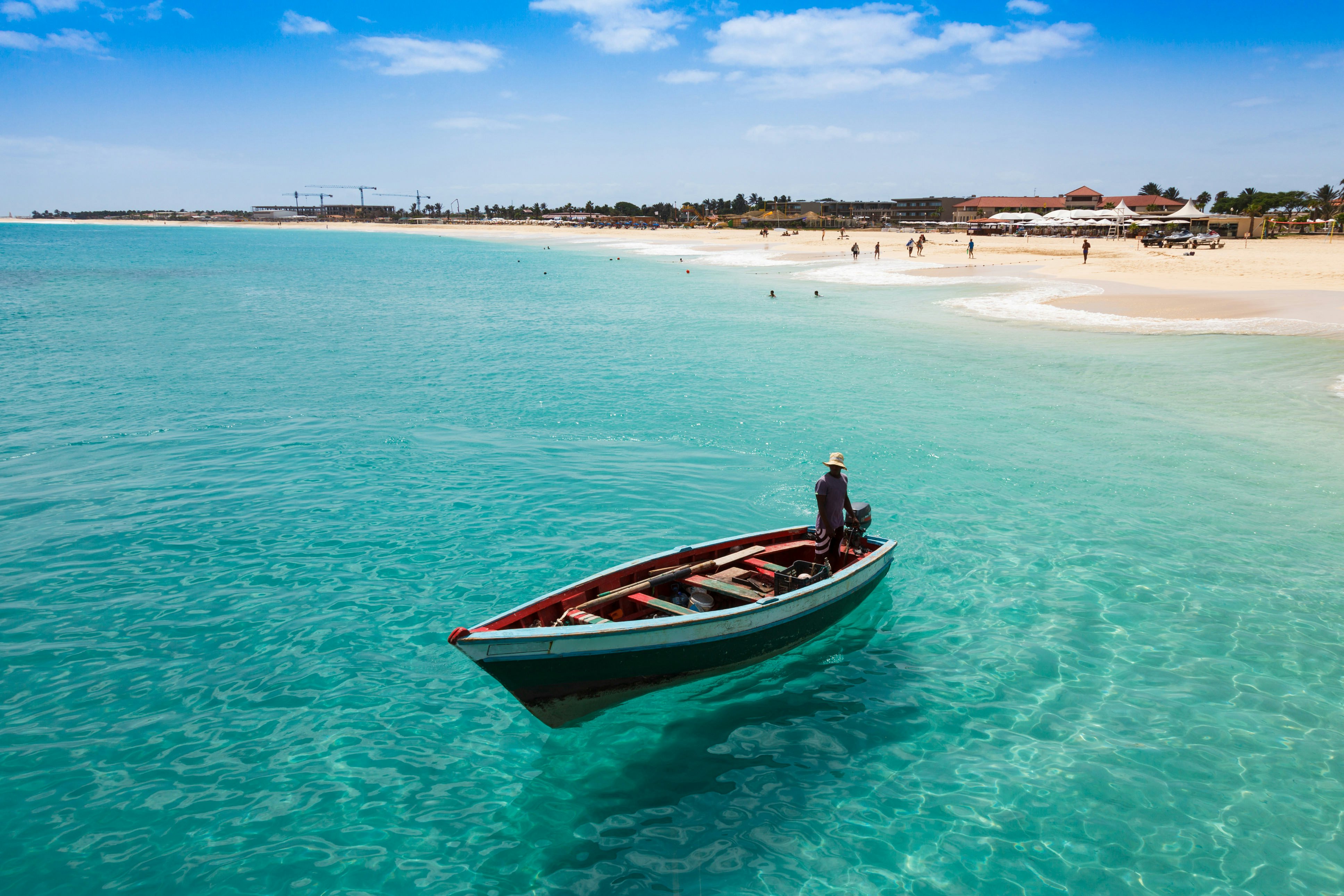 A fishing boat is seen in the shallow azure waters off a wide beach.