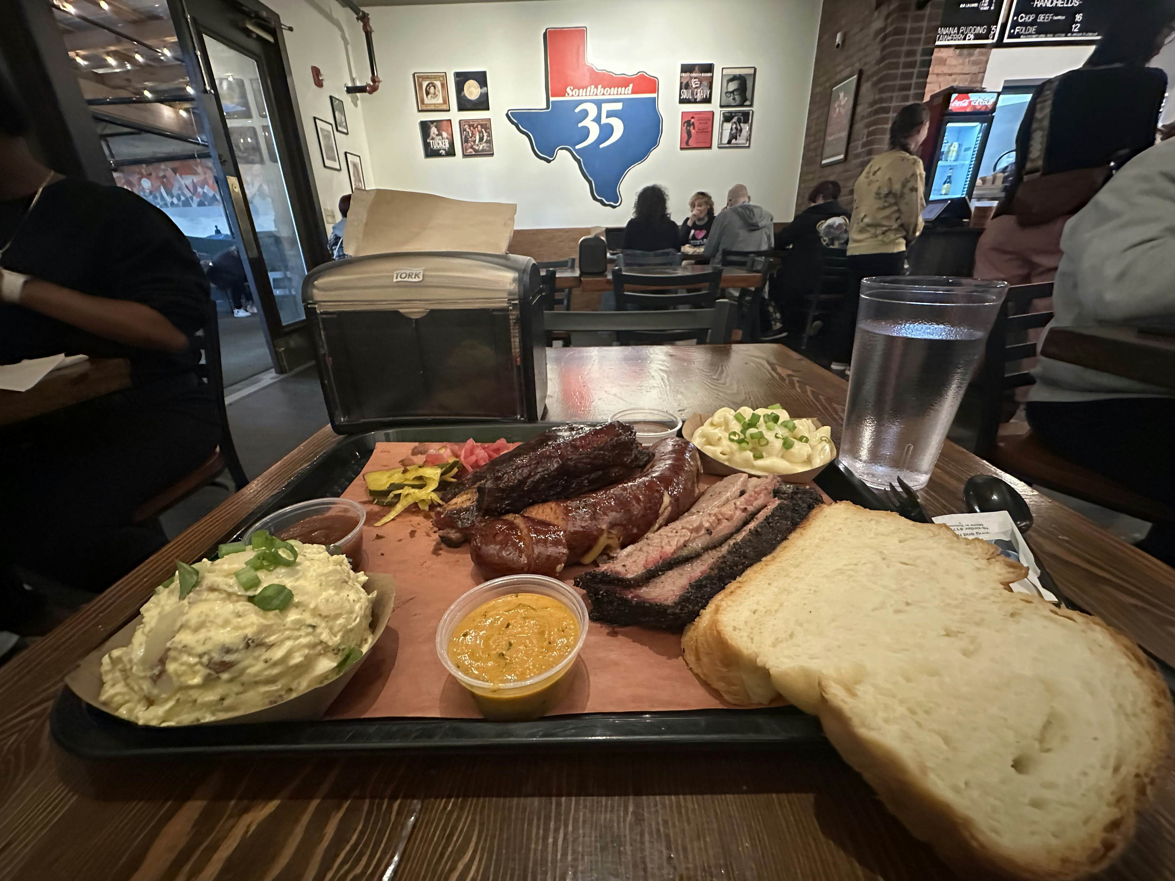 Tray of food with sausage, brisket, pork ribs, bread and potato salad. 