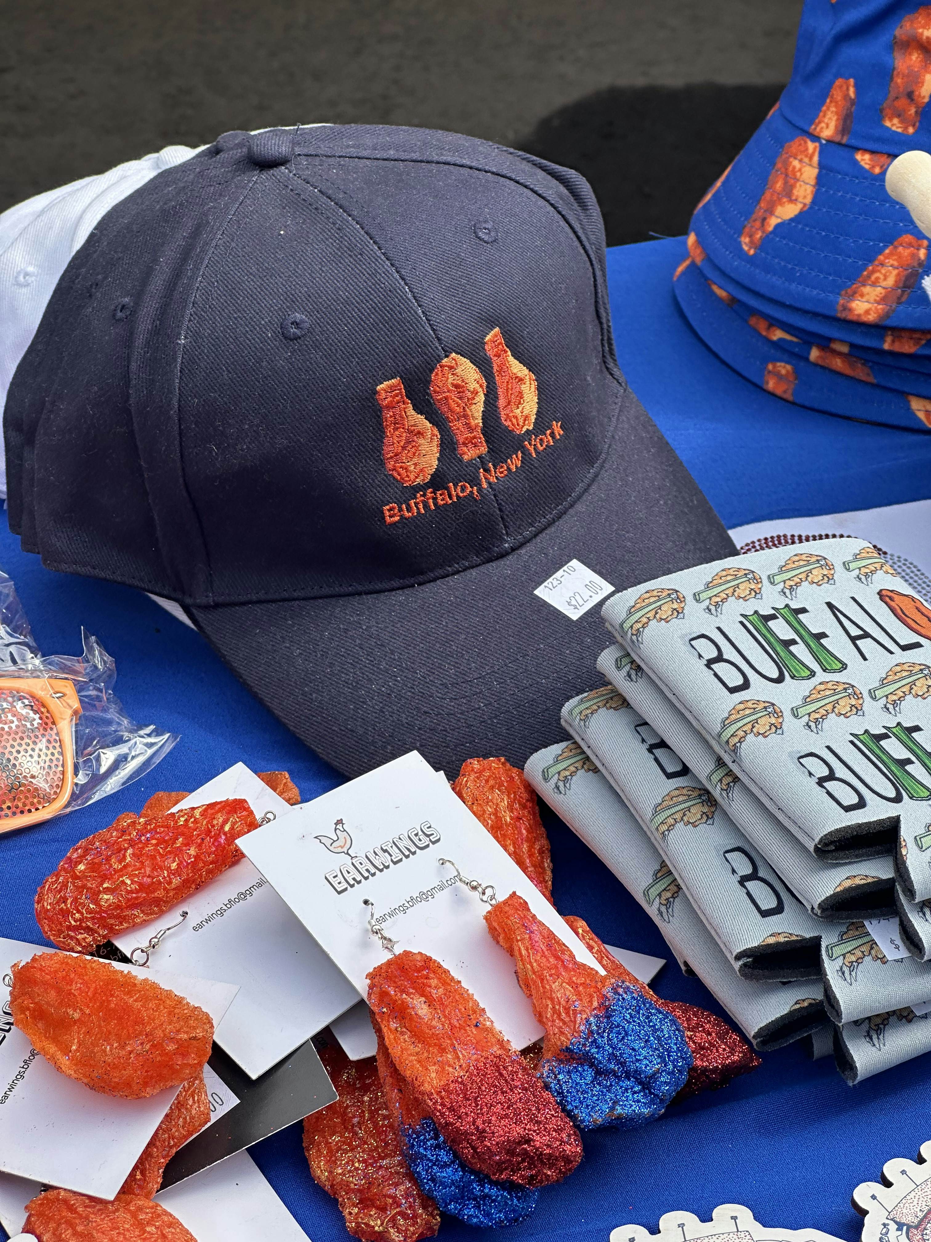 Blue hat embroidered with an orange chicken wing, life sized chicken wing earrings with glitter and a beer koozie