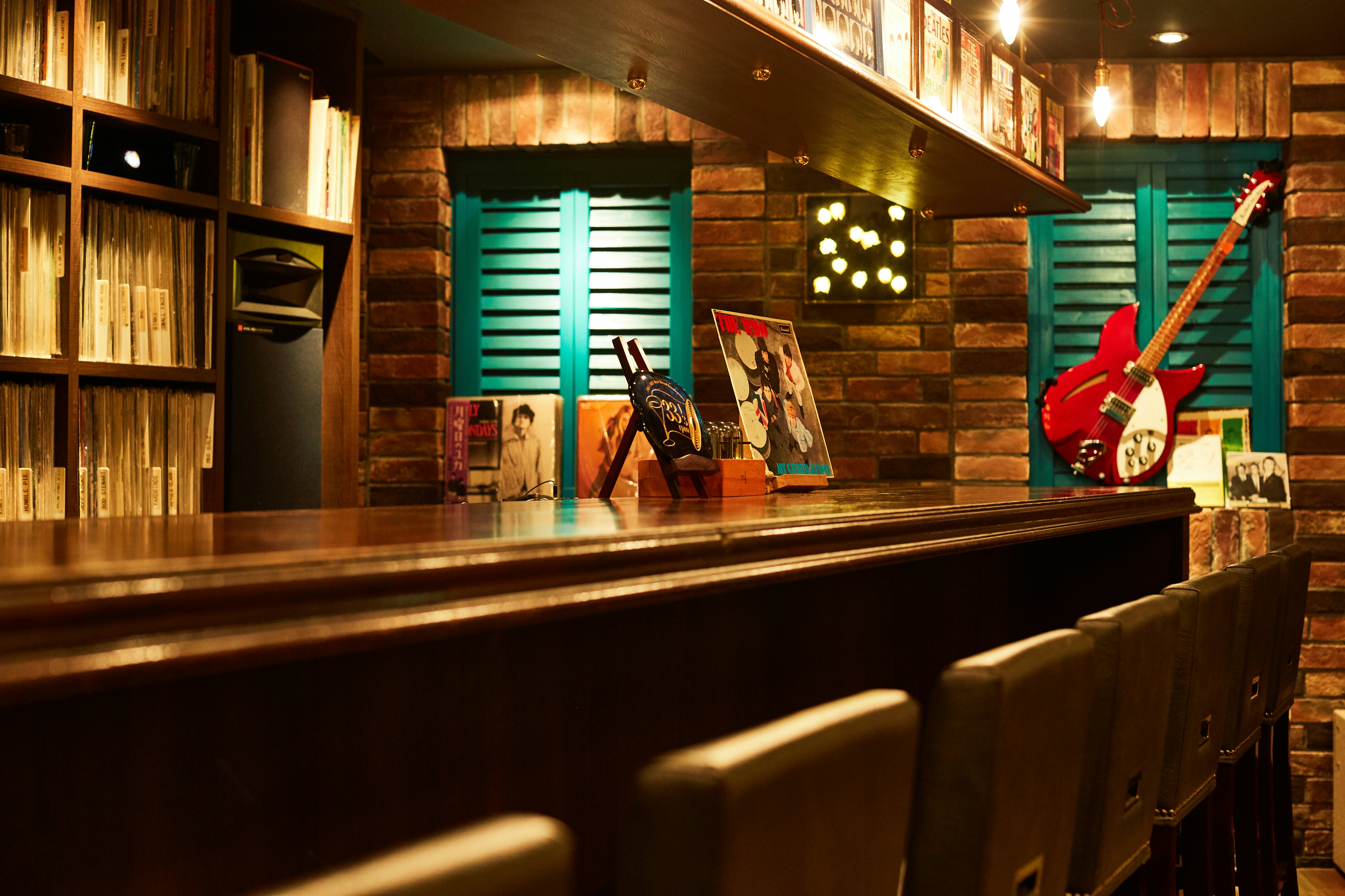 Stools lined up neatly at a bar with a guitar mounted on the wall and album covers decorating the walls.