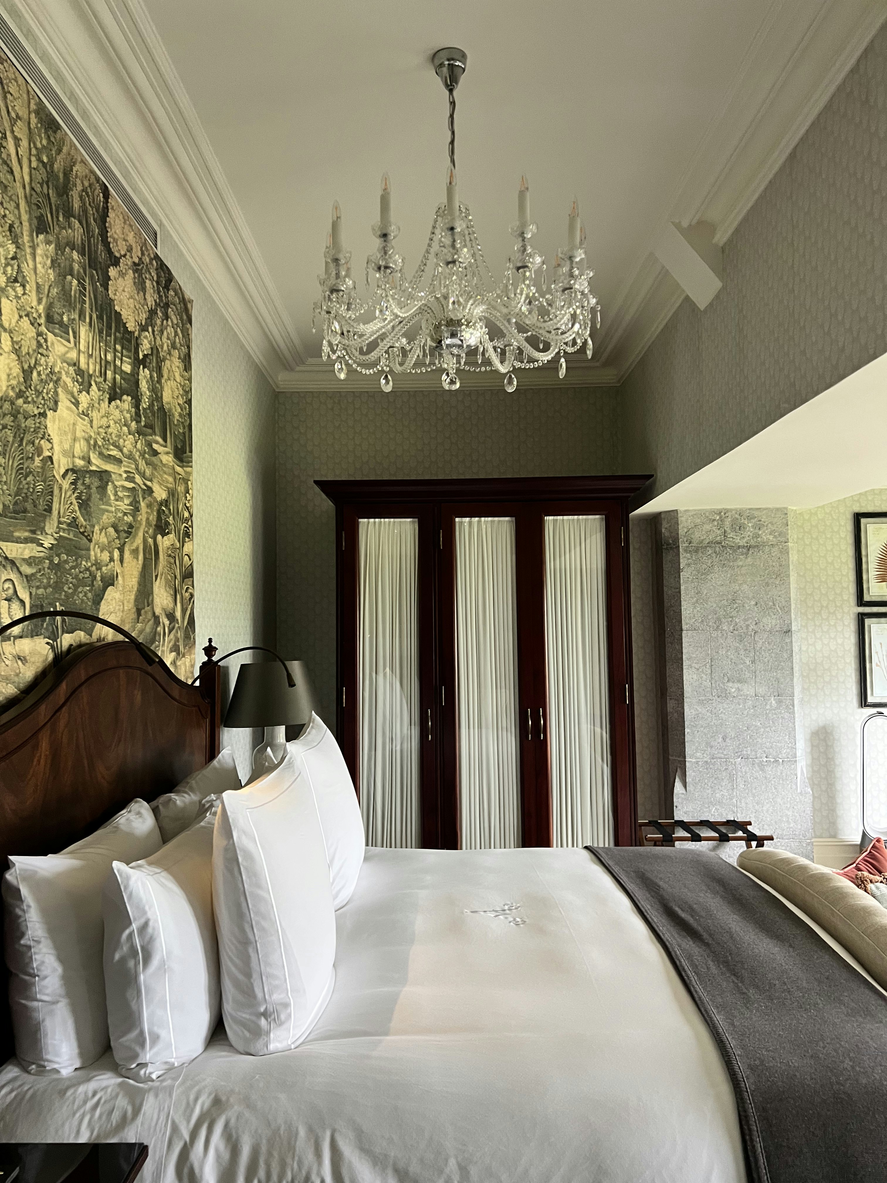 A king-sized bed in a hotel room with a glass chandelier hanging above it.