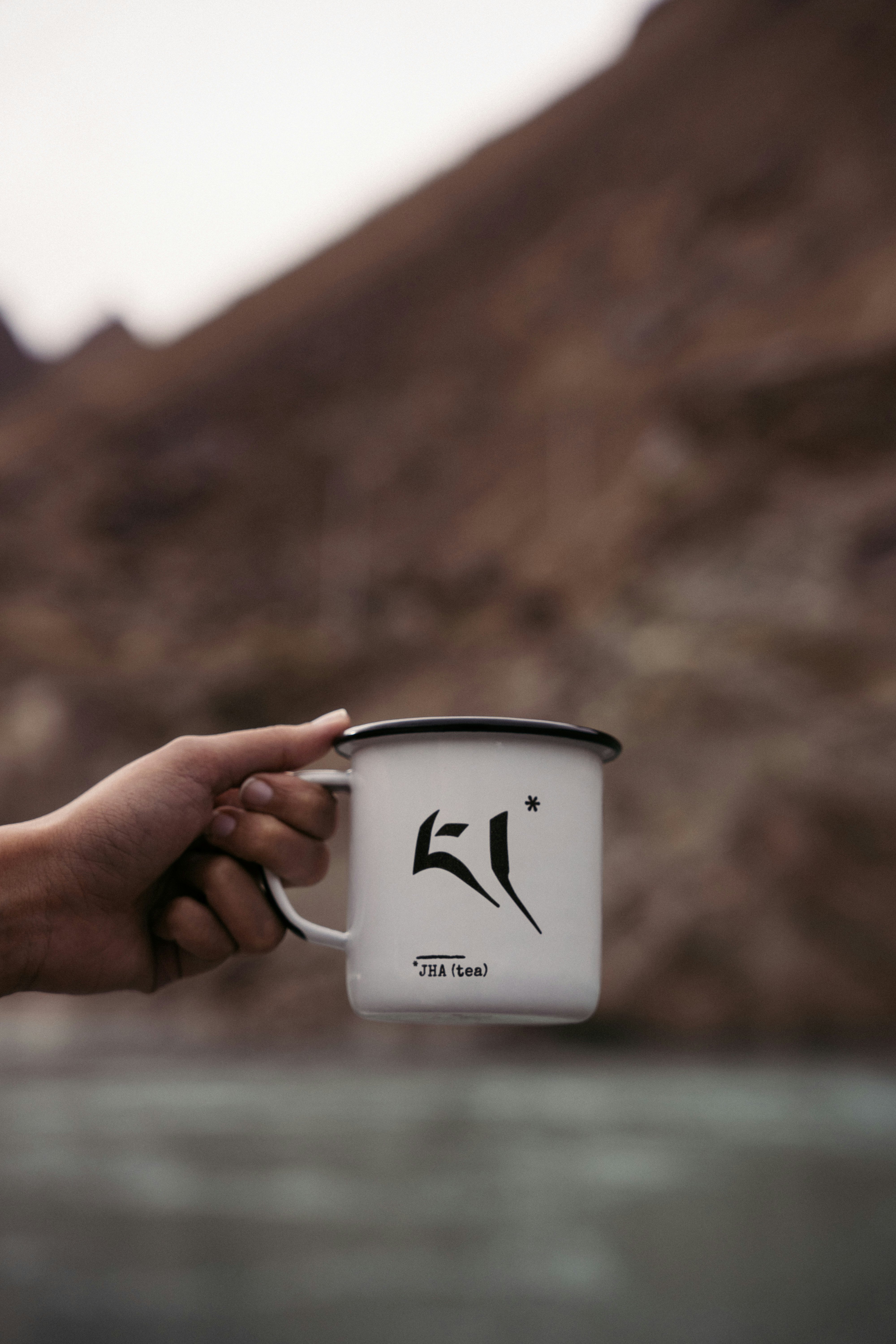 A hand holding a mug that says "JHA (tea)" on it.