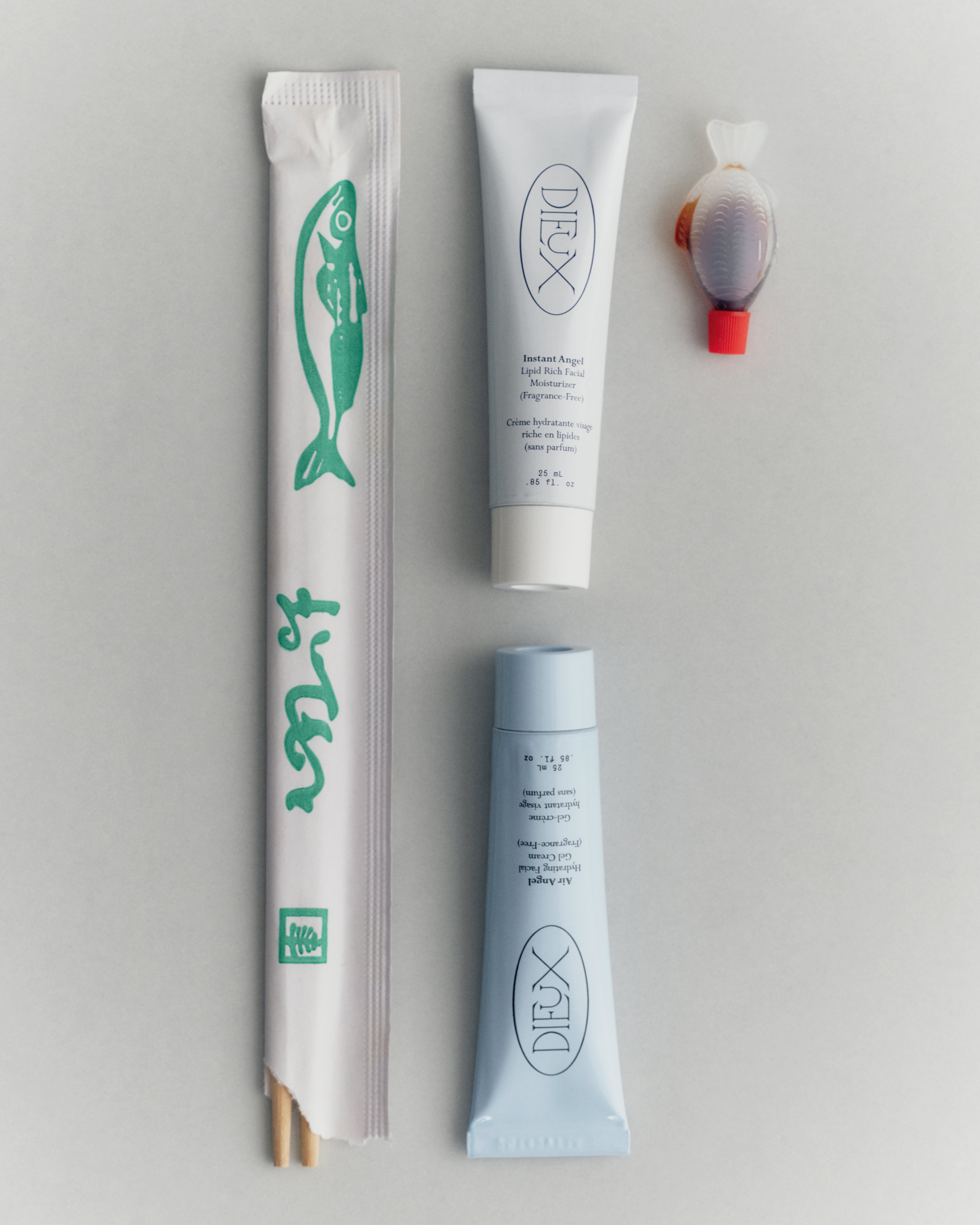 Two mini skincare products in tubes are lined up against a soy sauce in a fish bottle and chopsticks for scale