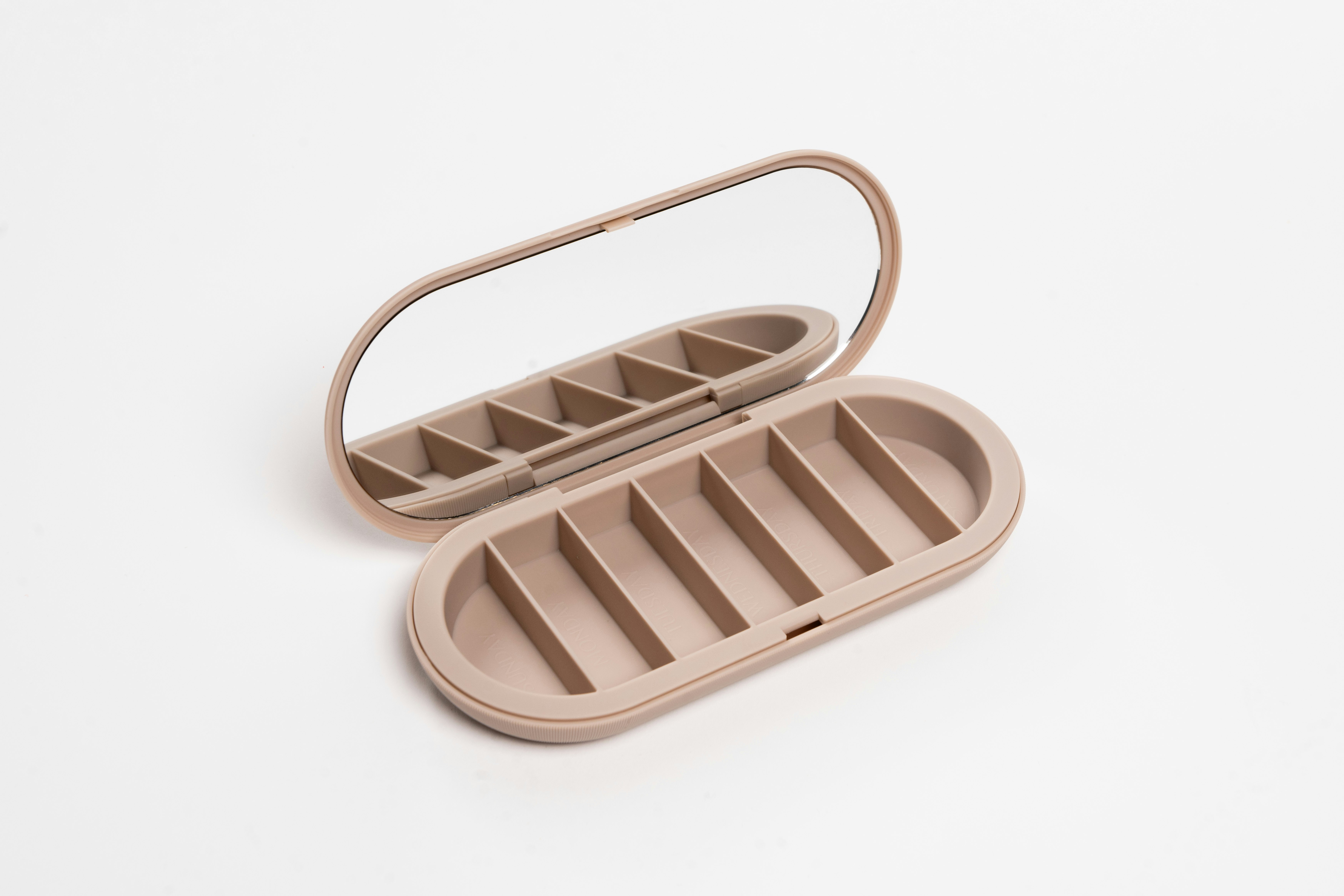 A tan oval-shaped container with seven compartments and a mirror.