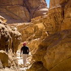 A hiker in red shemagh scarf, black t-shirt and cream trousers hikes through a yellow-rock canyon in Egypt with rocks either side of him and a sliver of clear blue sky in the background.
731845013
Getty, RFE, Landscape, Outdoors, Nature, Canyon, Adventure, Adult, Standing, Eroded, Summer, Travel, Lifestyles, Desert, Hiking, Geology, Egypt, Cliff, Day, Exploration, Sky, People, Mountain, Scenics, Tranquility, Men, Beauty In Nature, Full Length, Horizontal Image, Leisure Activity, One Man Only, One Person, Physical Geography, Real People, Rear View, Rock - Object, Rock Formation, Rocky Mountains, Tranquil Scene, Adventure, Canyon, Hiking, Leisure Activities, Mountain, Nature, Outdoors, Person, Valley
A hiker in a desert canyon in Egypt.