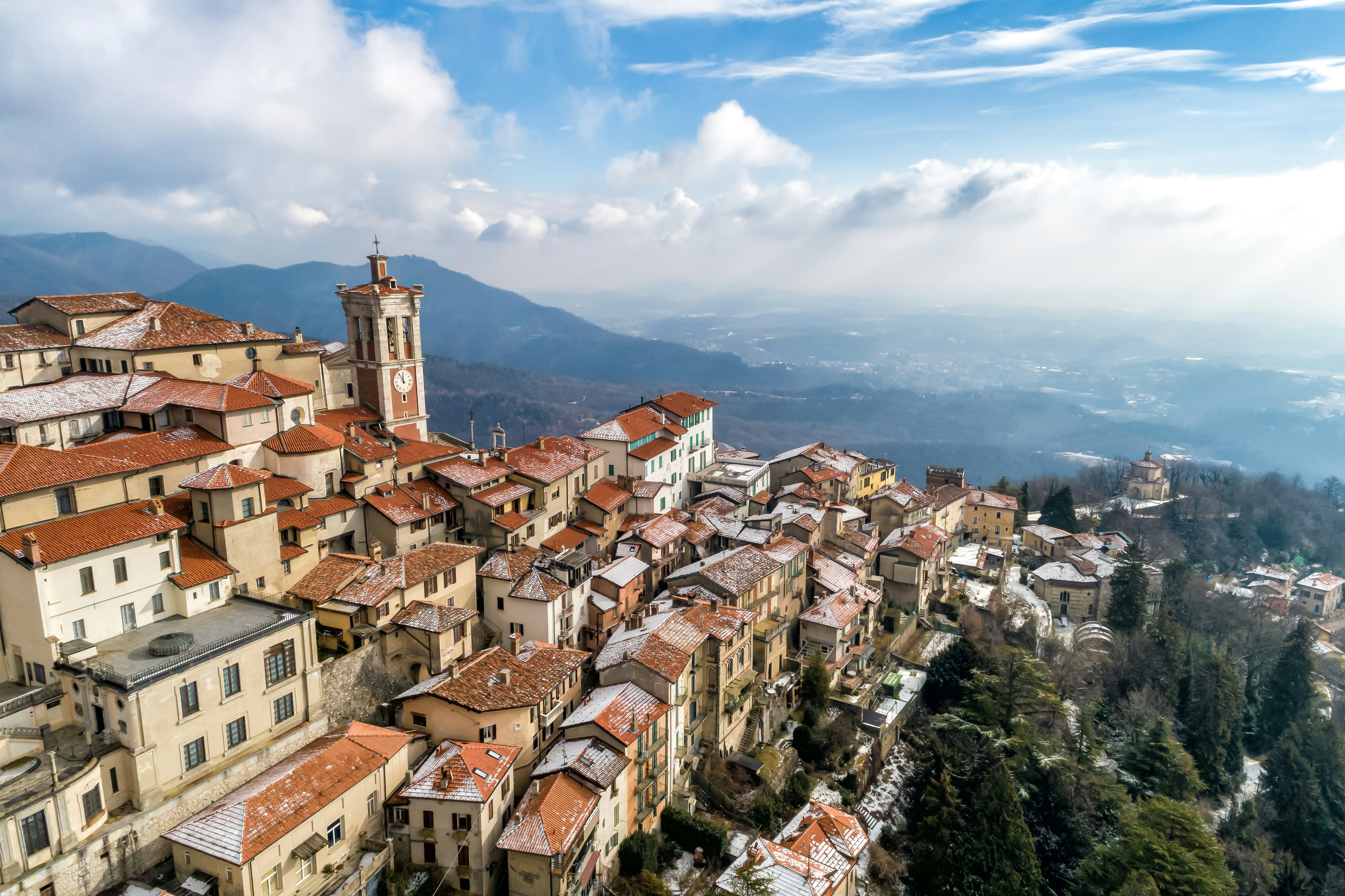 Aerial shot of a hilltop town with terracotta roofs overlooking a forest