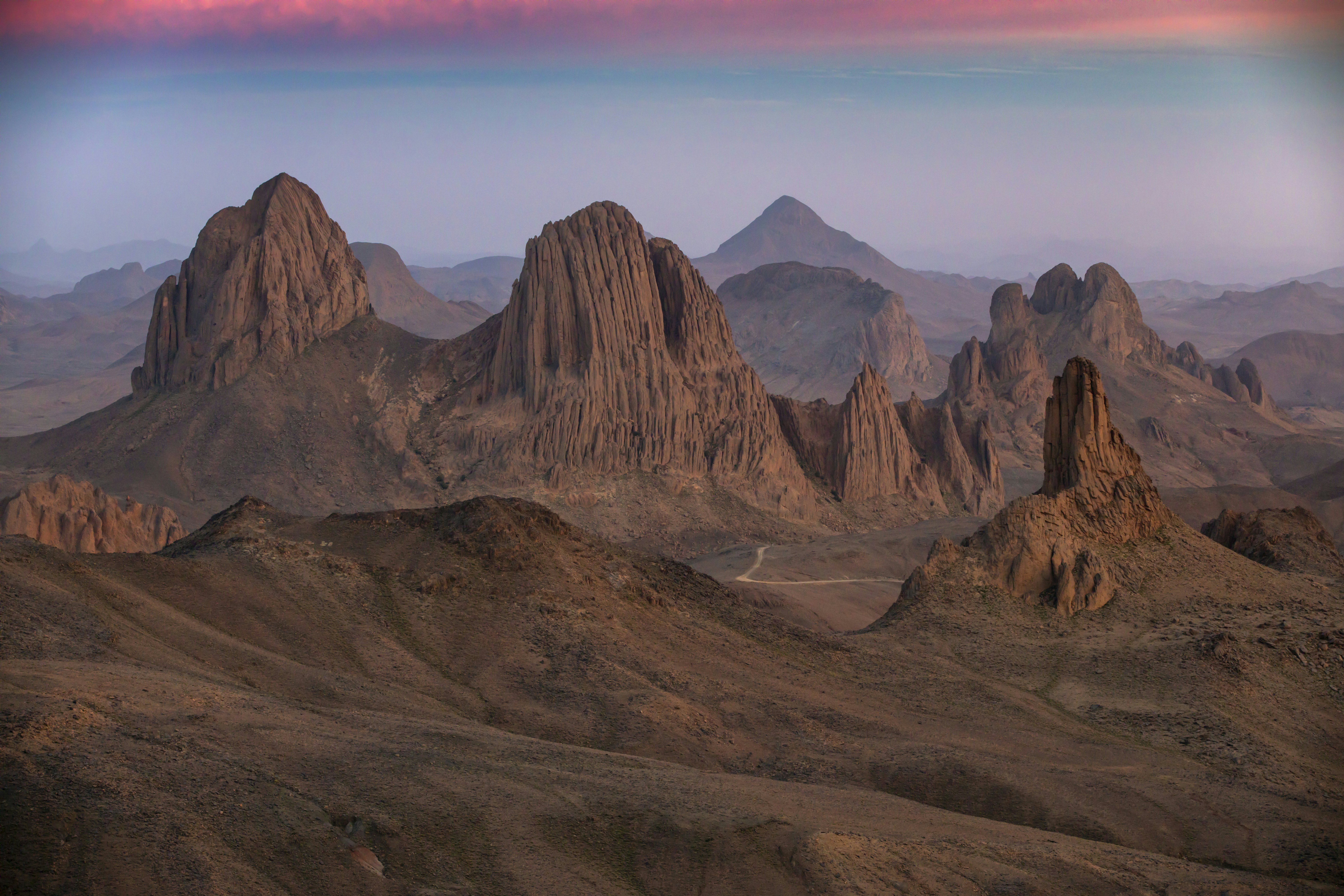 Rugged mountain peaks in a desert as the light fades casting a pink glow across the sky.