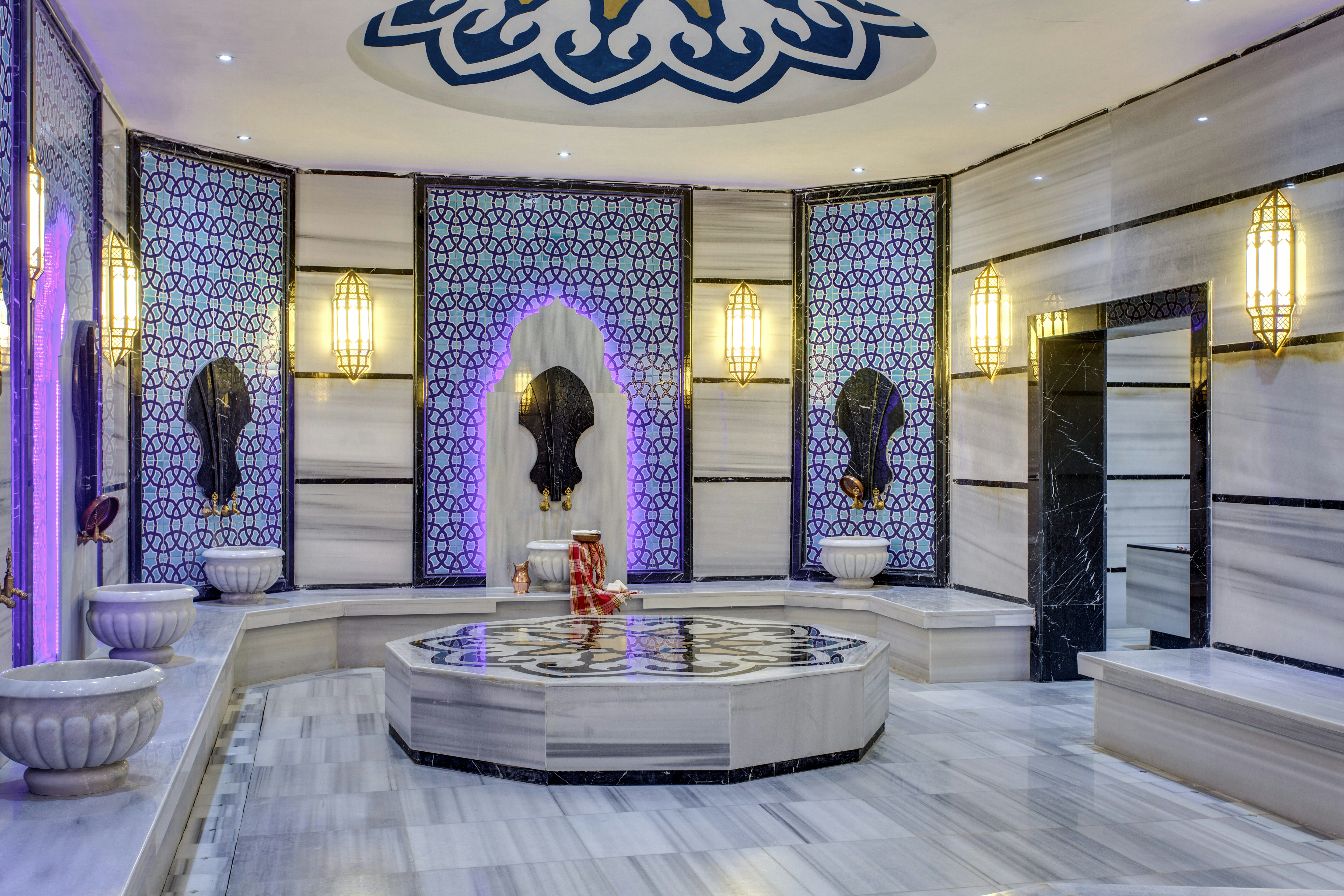 A marble room with built-in benches along the perimeter and a large central platform; there are patterned alcoves on the wall, and black accents on the doorway and benches.