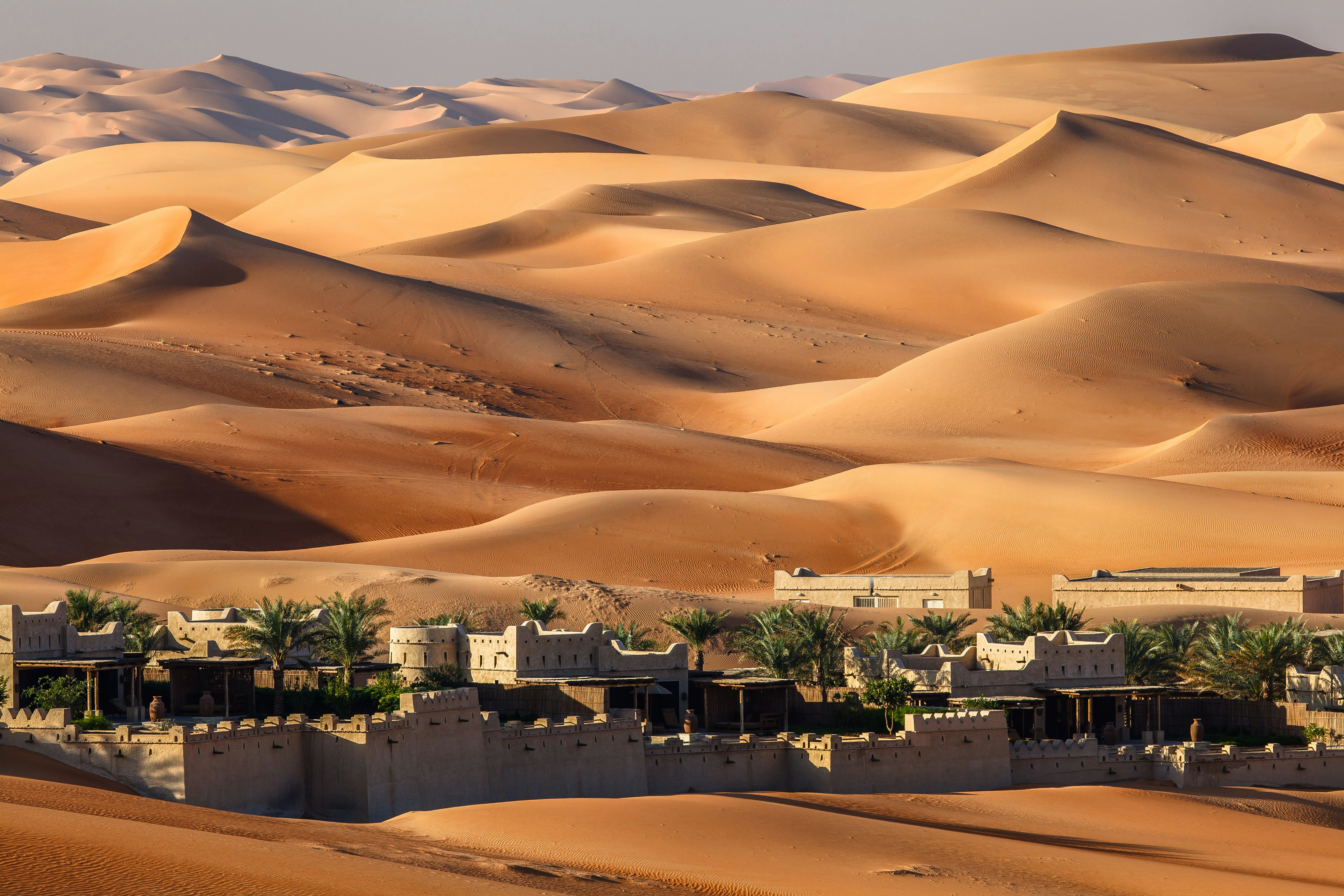 A fortified desert town at the foot of vast sand dunes.