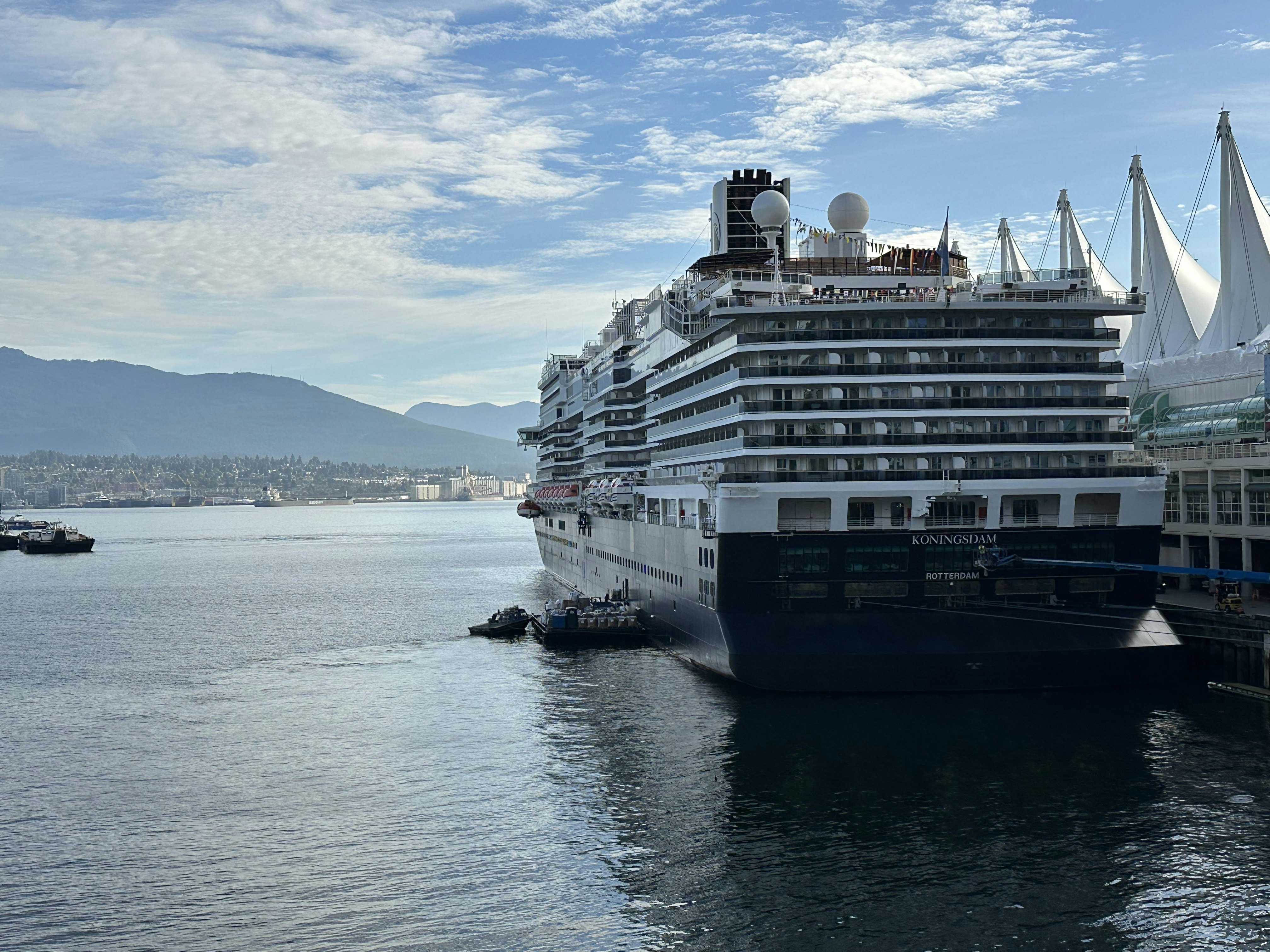 A cruise ship at port on a sunny day with low mountains in the distance.