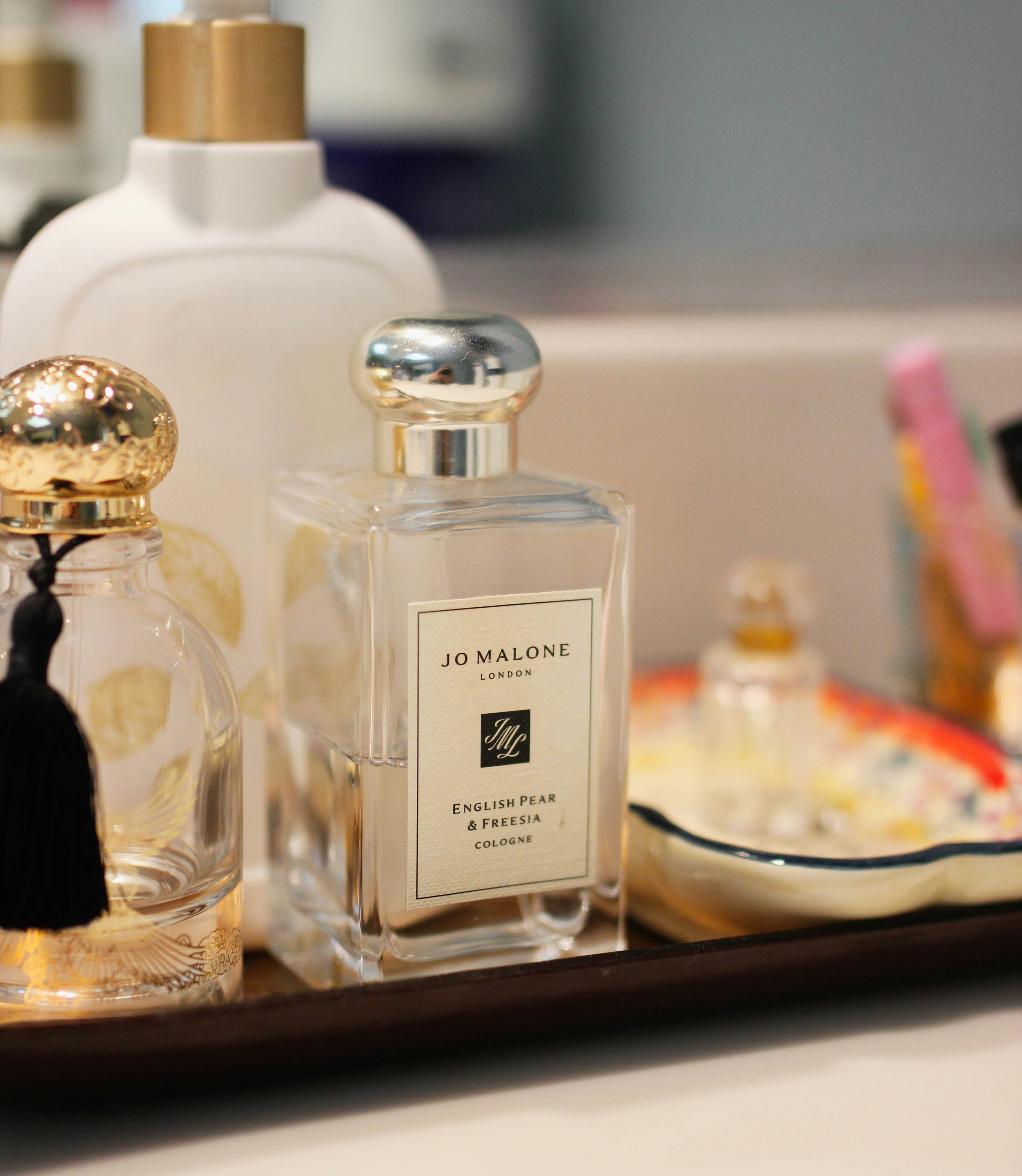A perfume stand that is holding two bottles of perfume. One is a vintage-style perfume with a tassle, while the other is a Jo Malone fragrance.