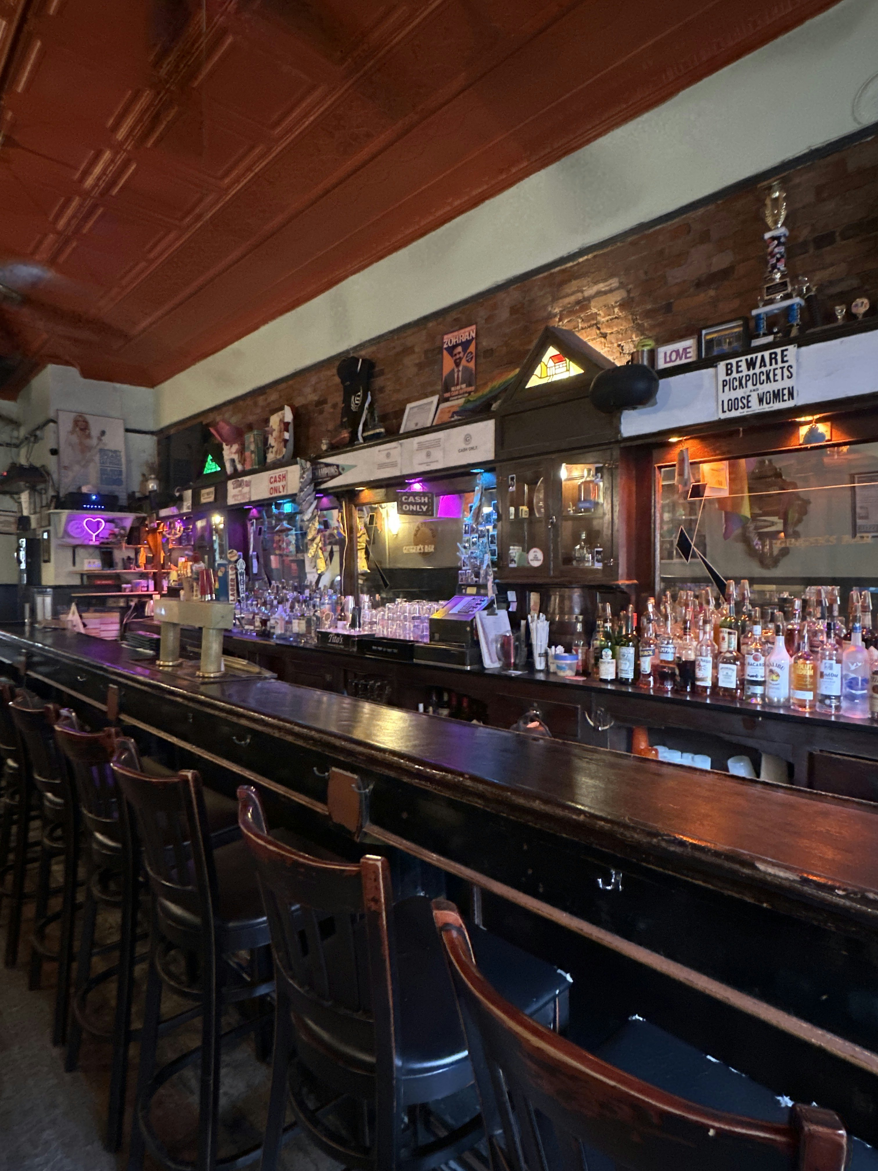 Dark bar stools are pulled up to a long, empty bar with bottles on the counter behind.