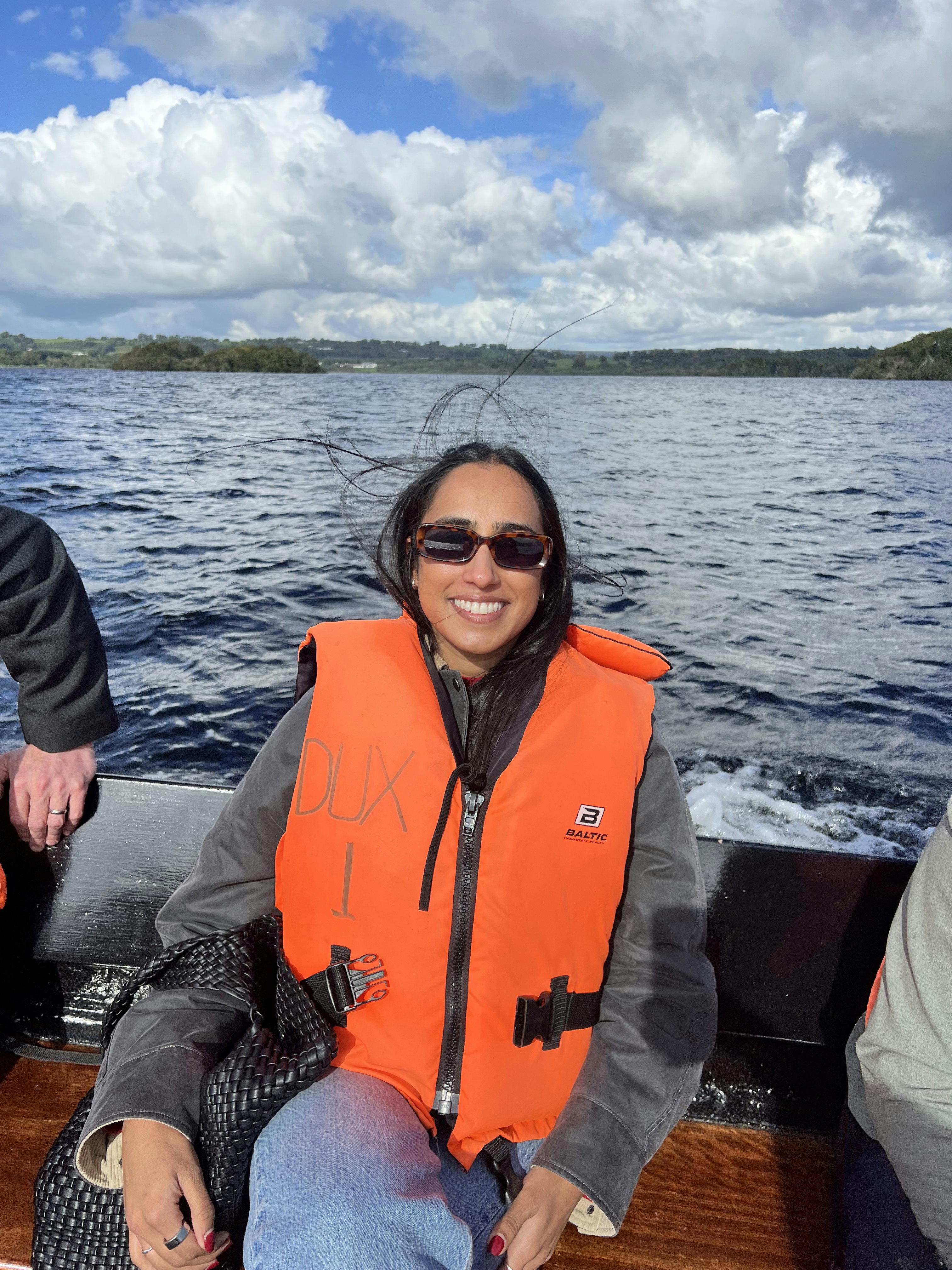 A woman on a small boat wearing a life jacket and smiling for the camera. Her hair is blowing in the wind.