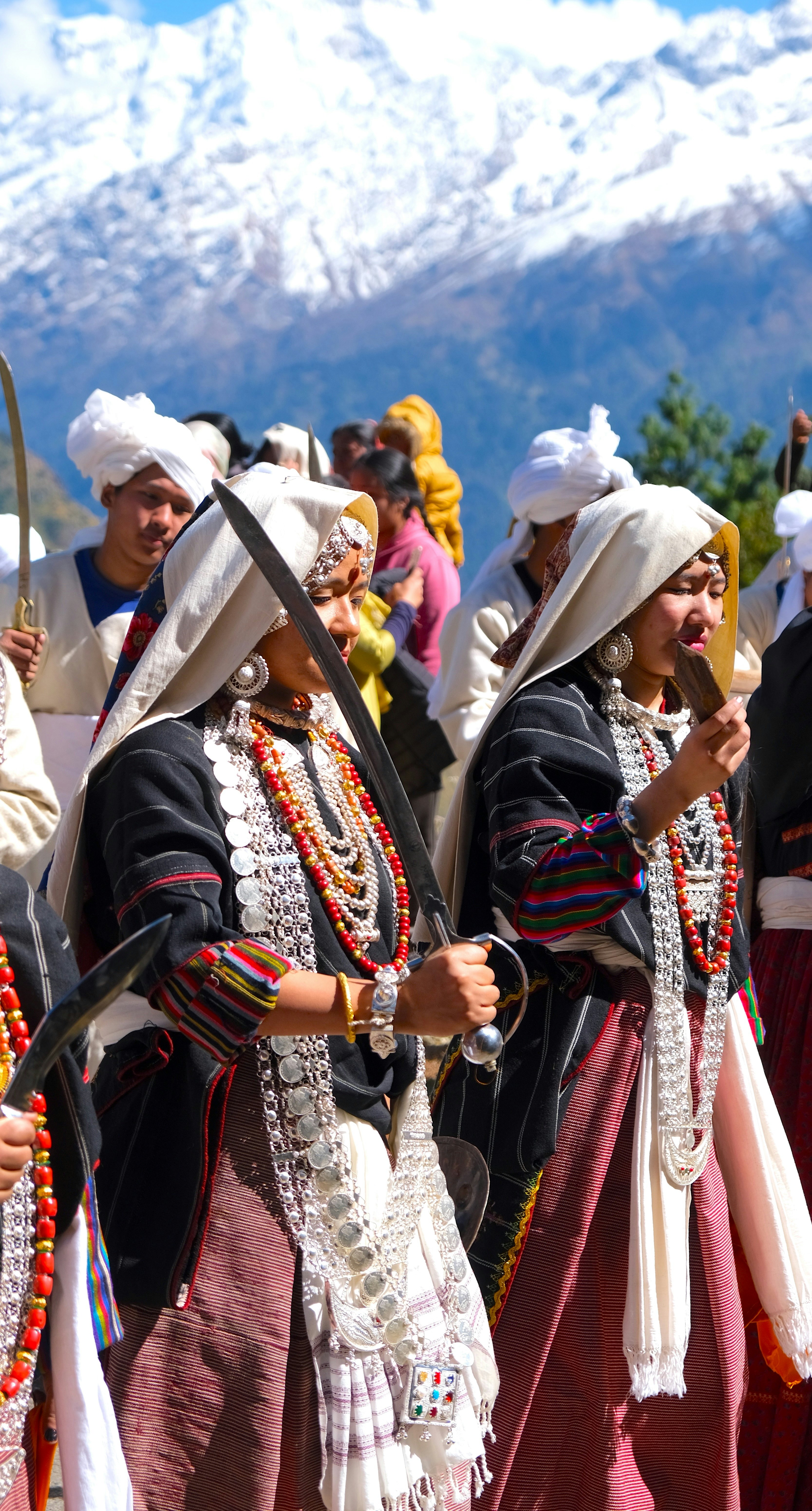 Two women in traditiona tribal dress at a festival in a mountain region. One is holding a sword.