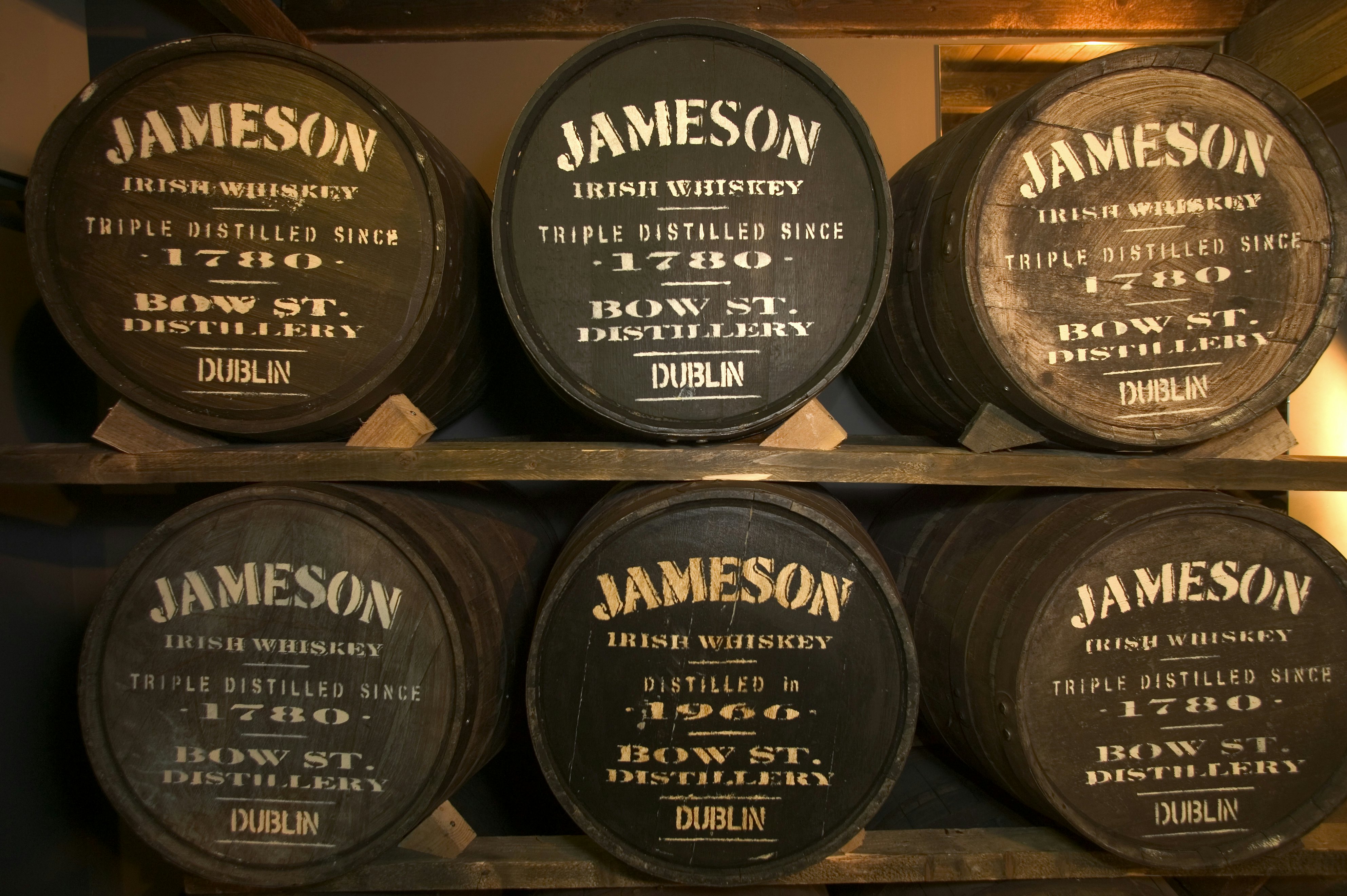 Two shelves hold six wooden barrels of Jameson whiskey stamped with information about the distilled date and location.