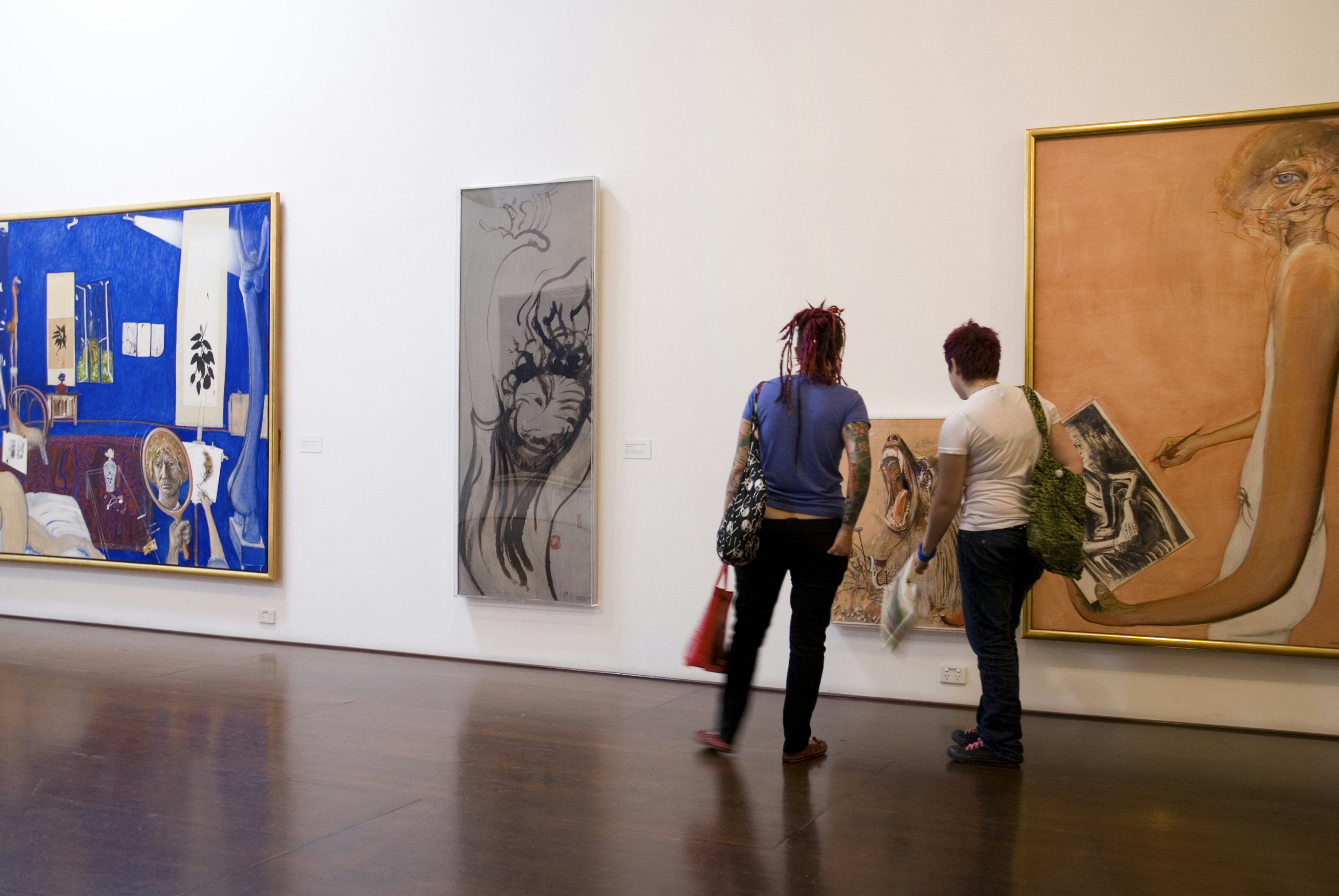 Two people admire paintings in a gallery.