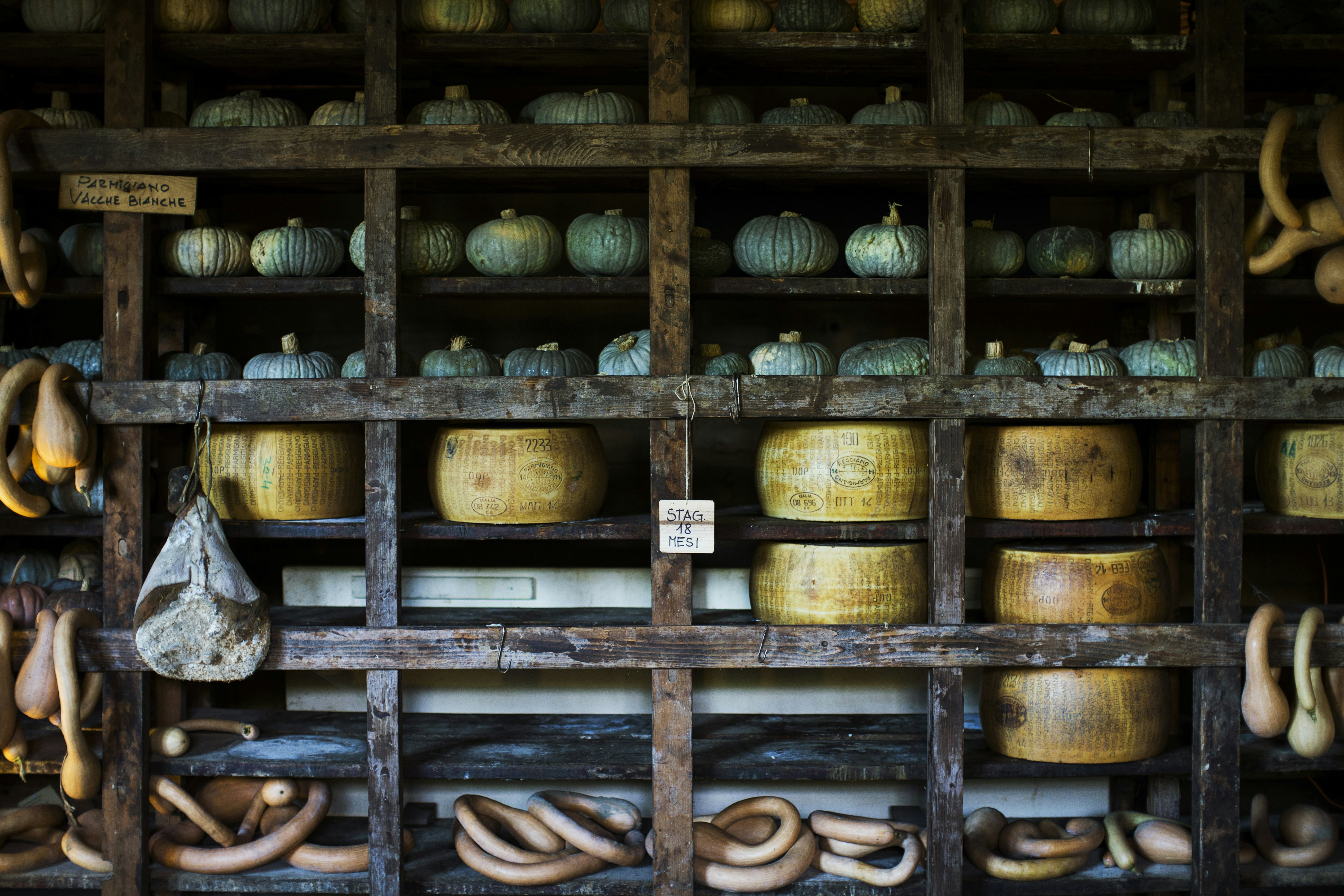 Wooden storage racks of pumpkins and Parmigiano Reggiano cheeses in Emilia-Romagna, Italy.