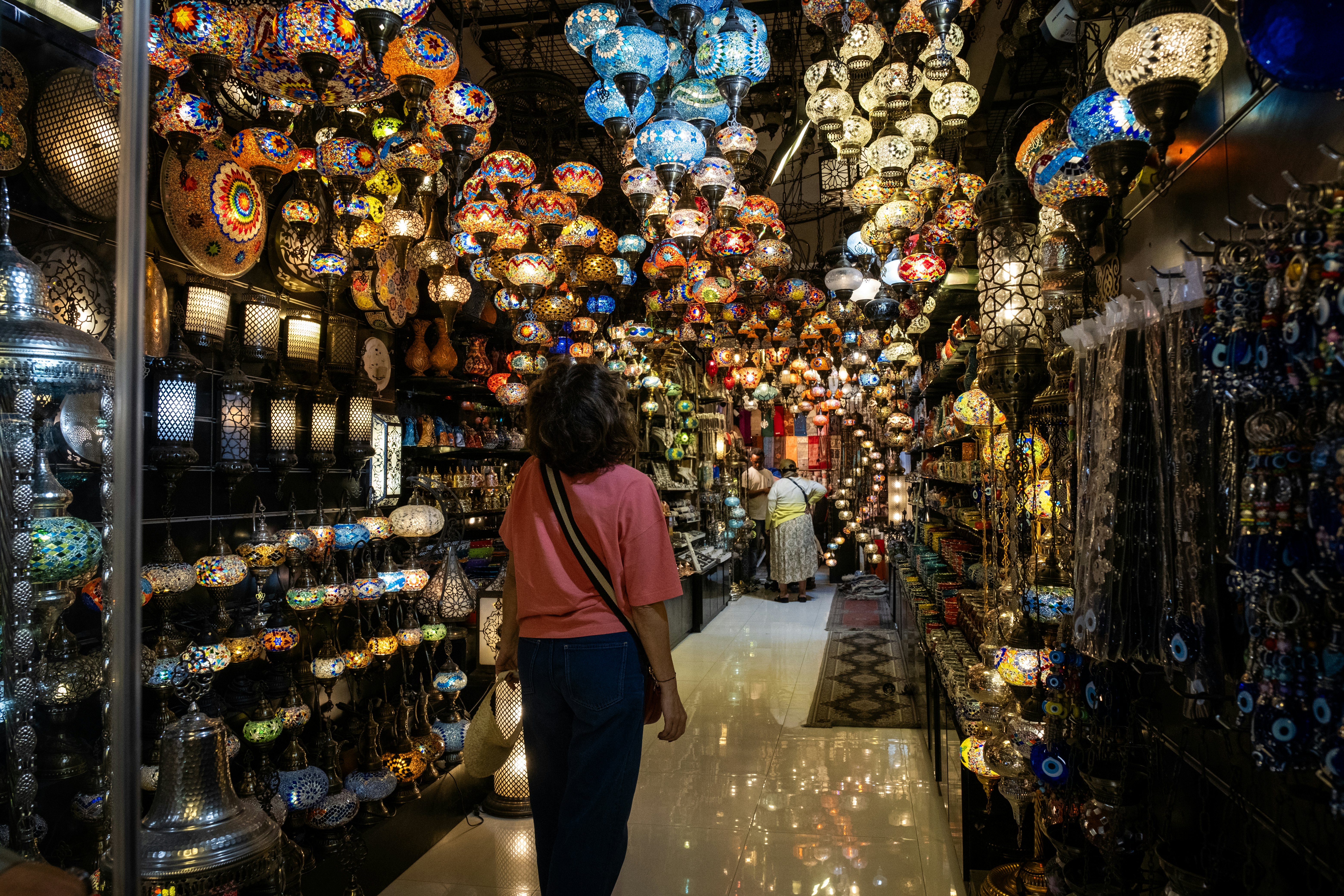 A woman walks among market stalls filled with lamps and other light fixtures.
