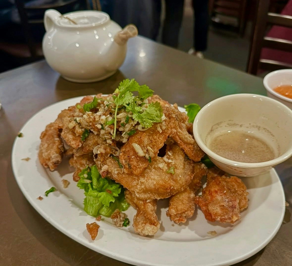 A white dish holding deep-fried chicken wings sprinkled with garnish.