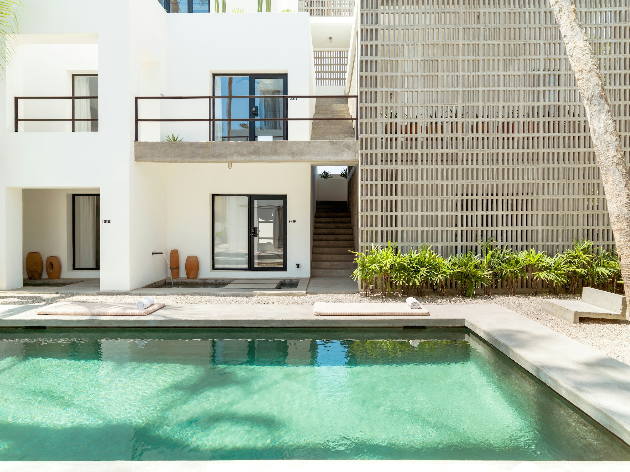 A pool is in front of a white building with a black door and small shrubs