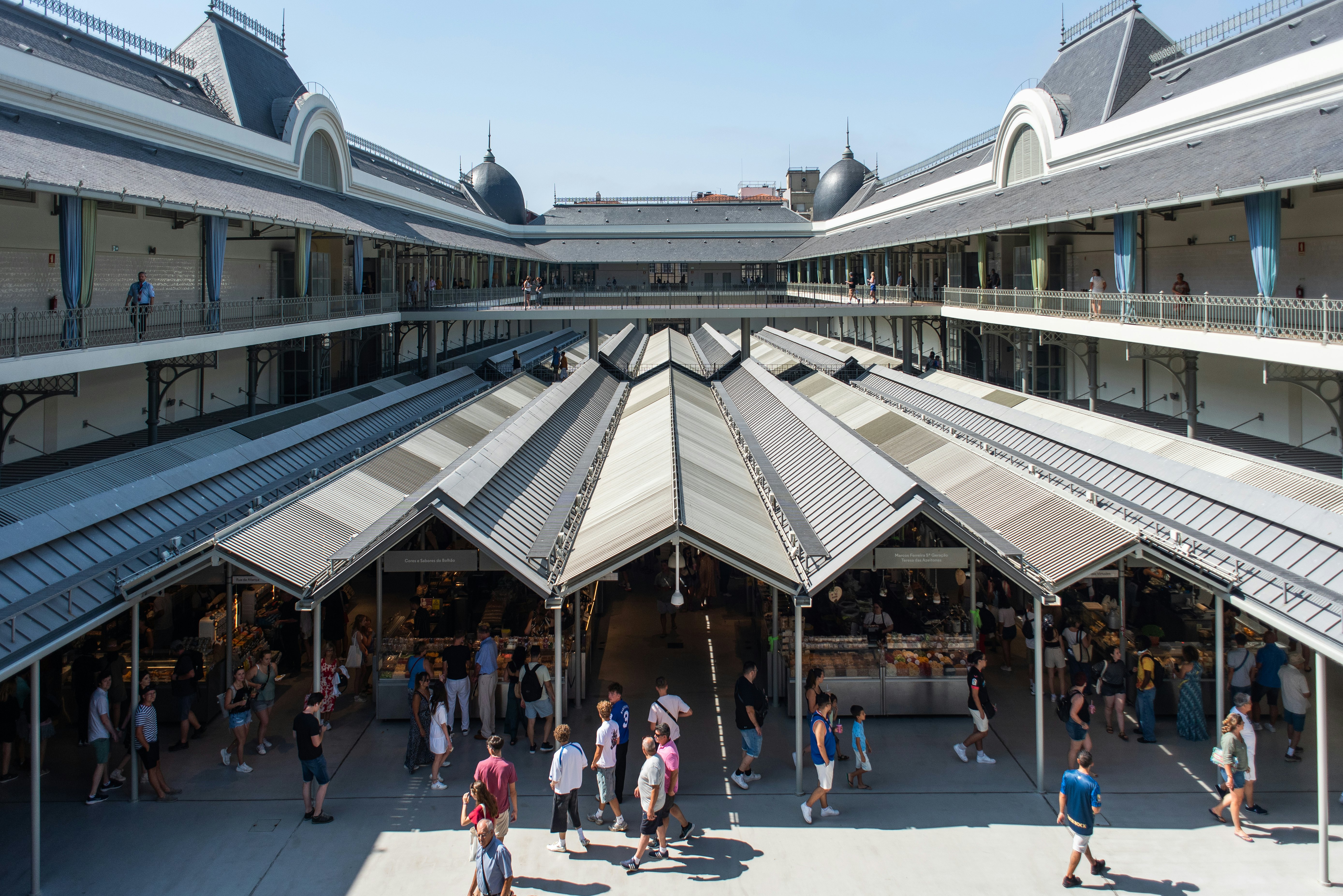 The pointed roof and walkways of a covered market busy with shoppers.