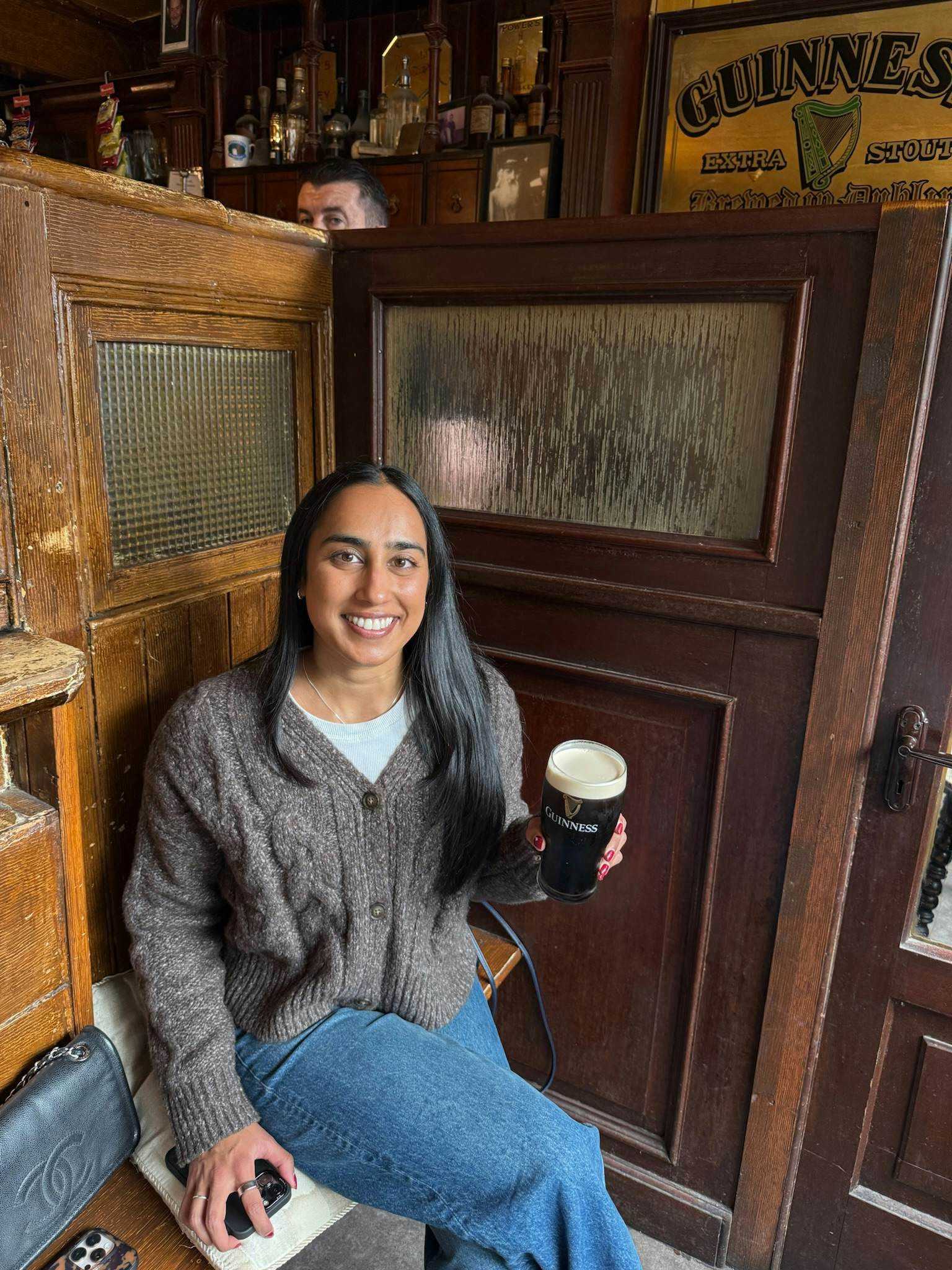 A woman sat in a pub with panelled walls holds a pint of Guinness, a black drink with a white foamy top.