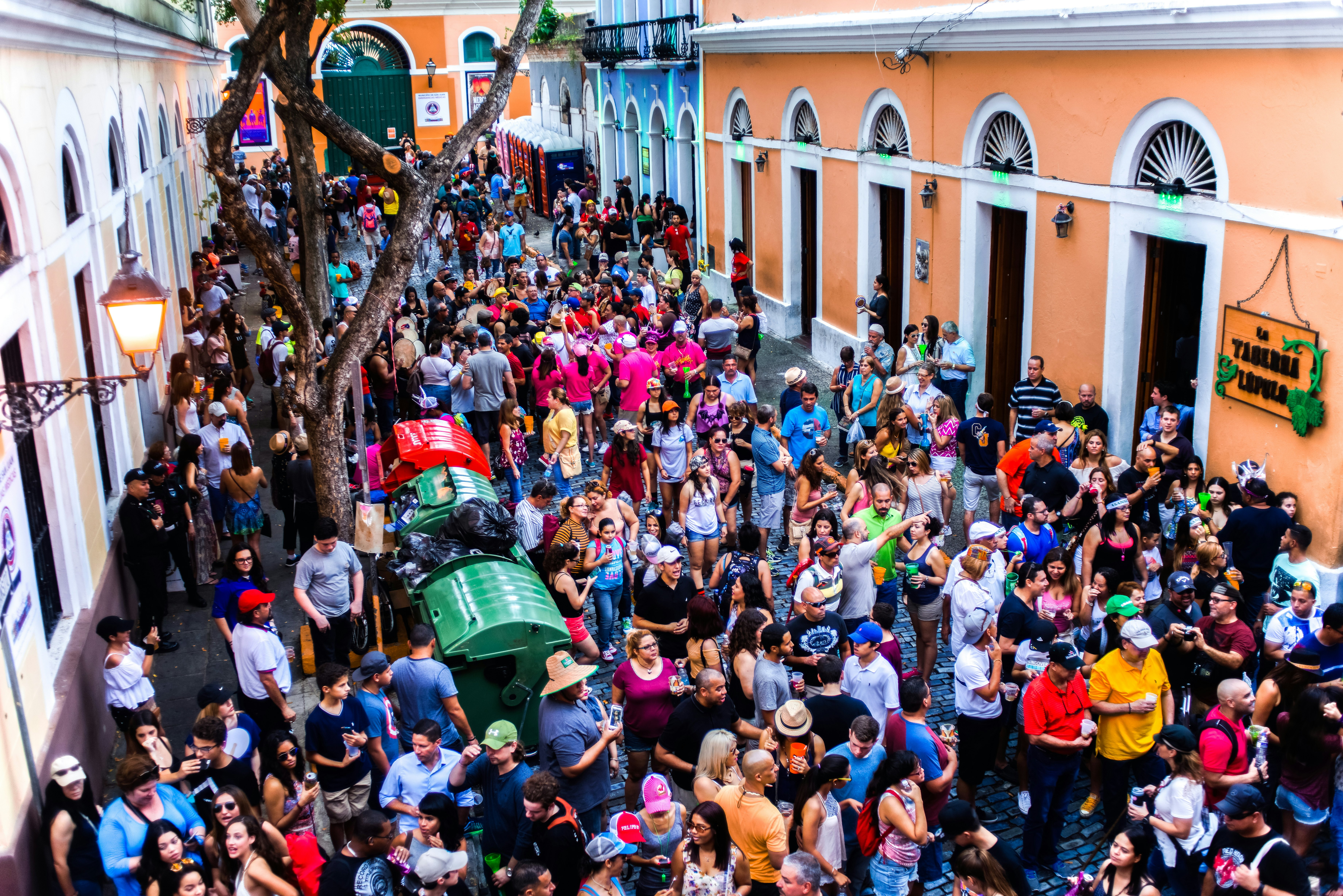A crowd of people fill a street lined with colorful buildings in Puerto Rico.