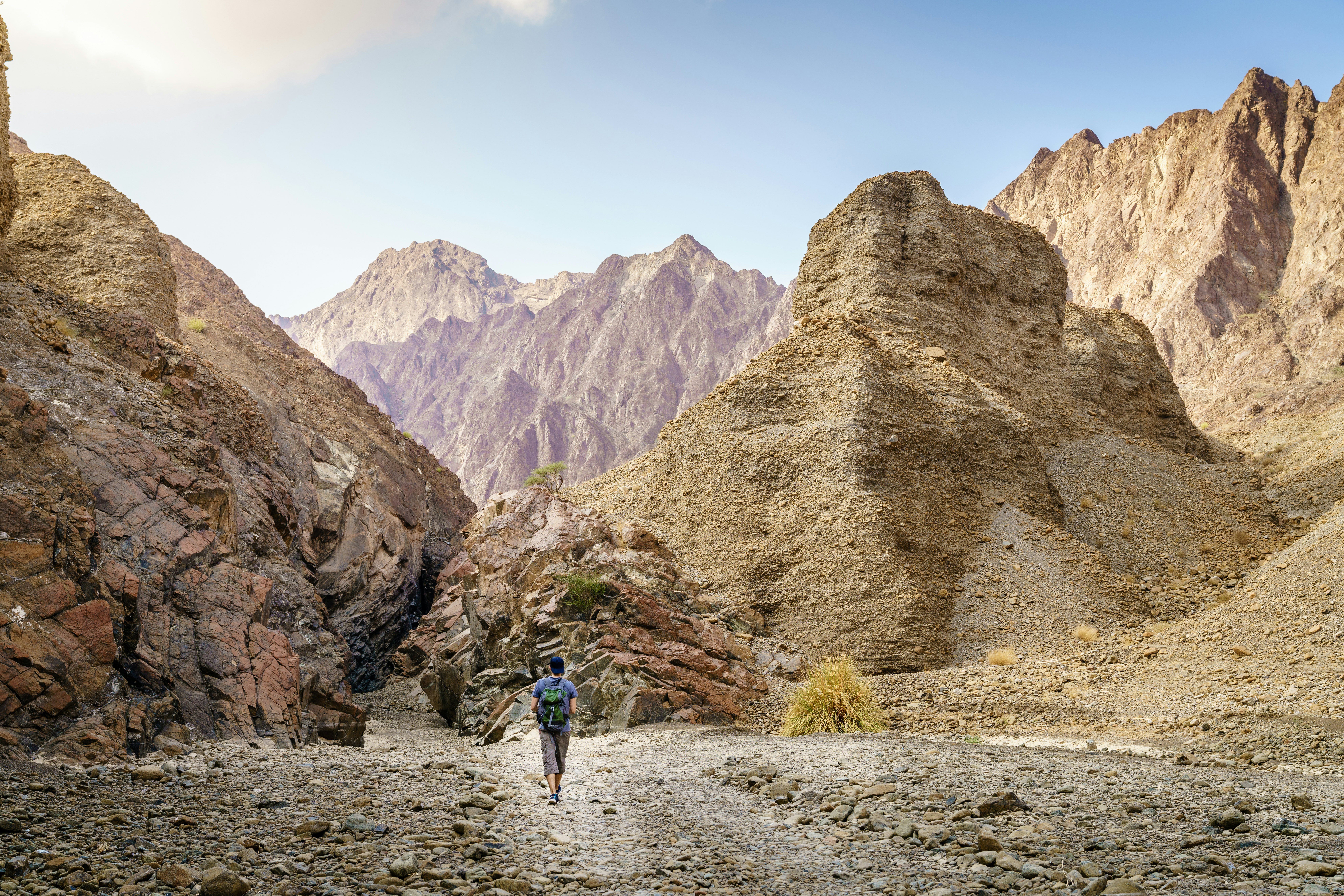 A hiker in a dry, rocky landscape walks toward peaks in the distance in the United Arab Emirates.
