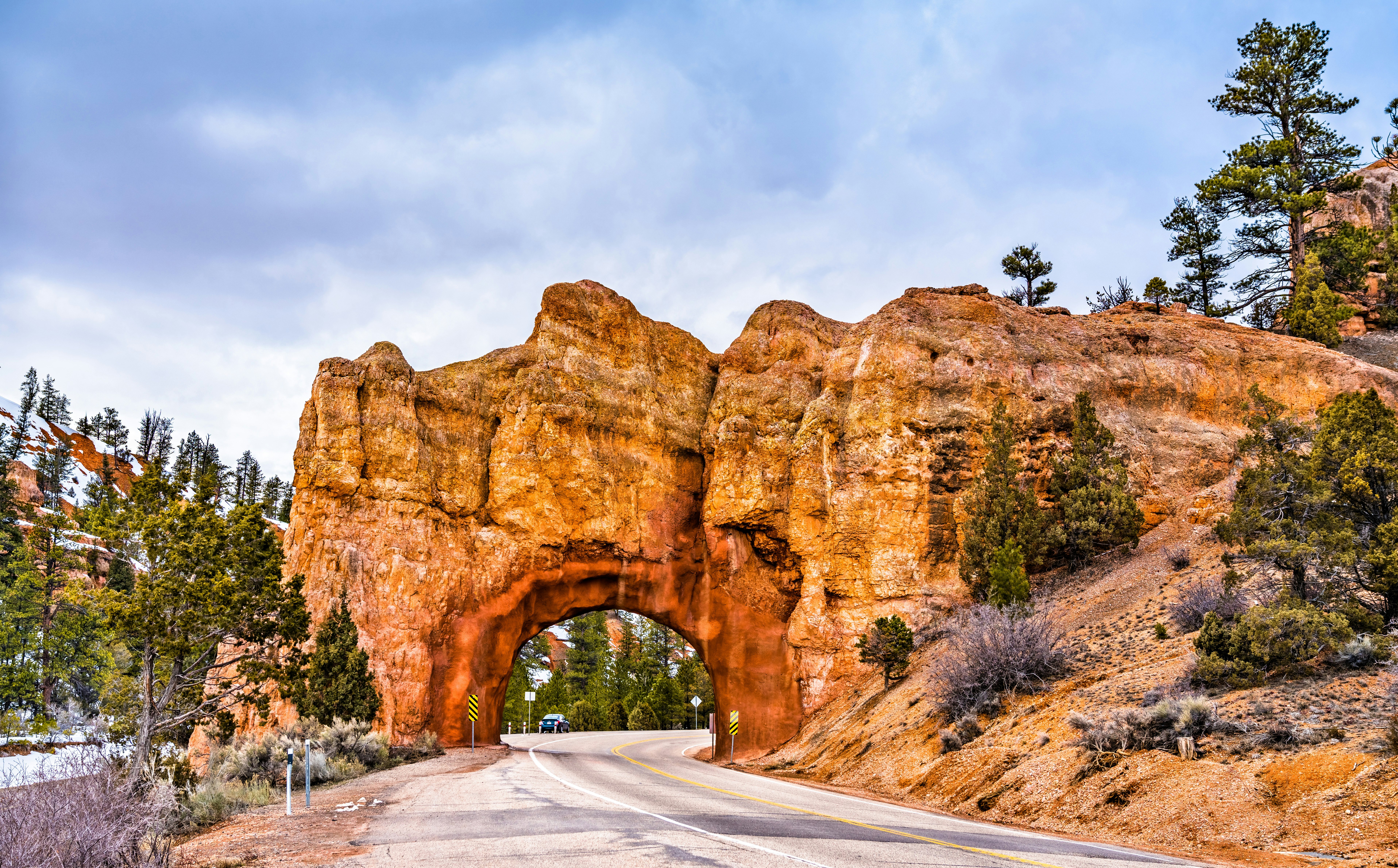 A road passing through a huge red-rock archway.