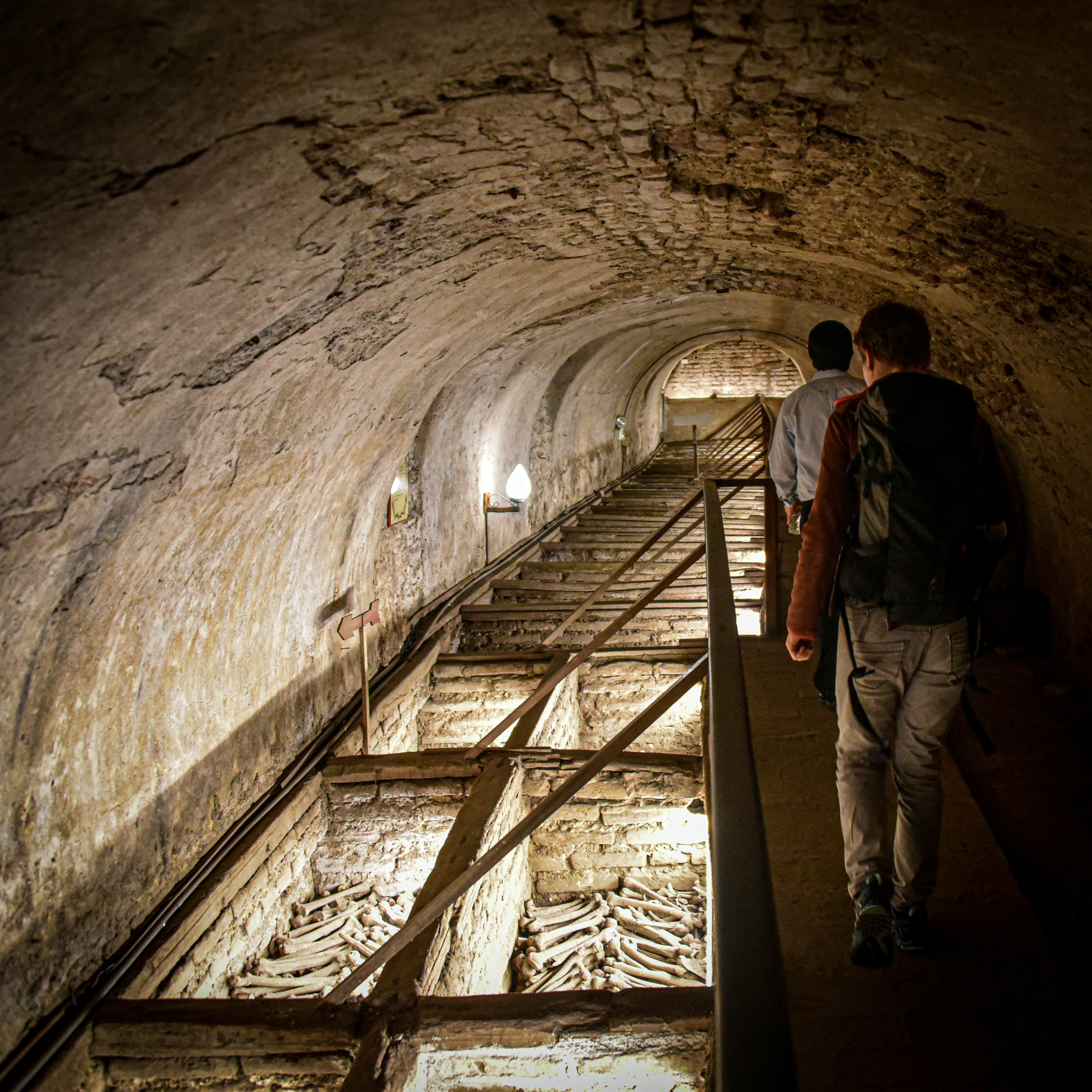 People walk on an underground catwalk over tombs that display hundreds of human bones.