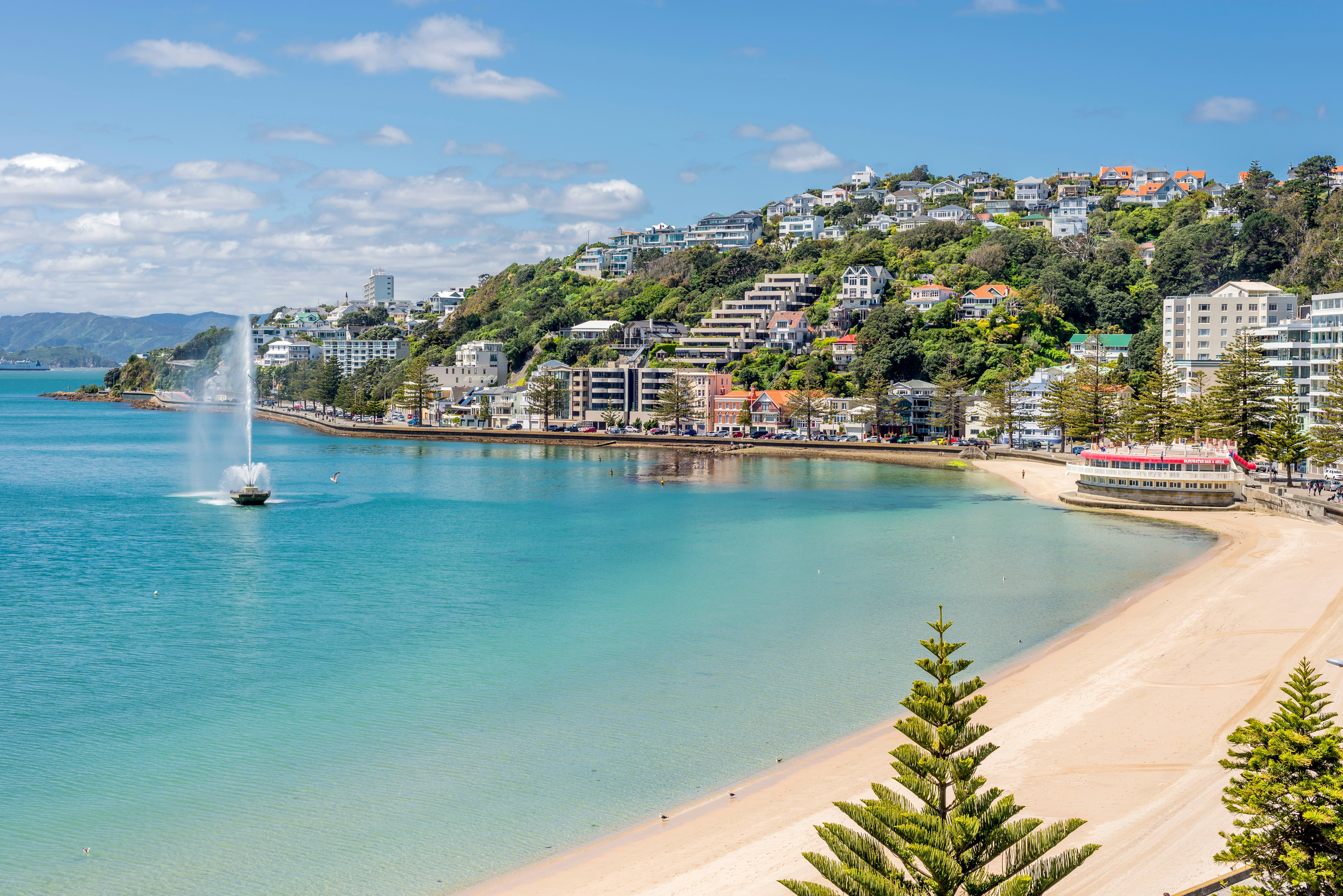 A city beach in a cove backed by hills covered in homes and businesses on a sunny day.