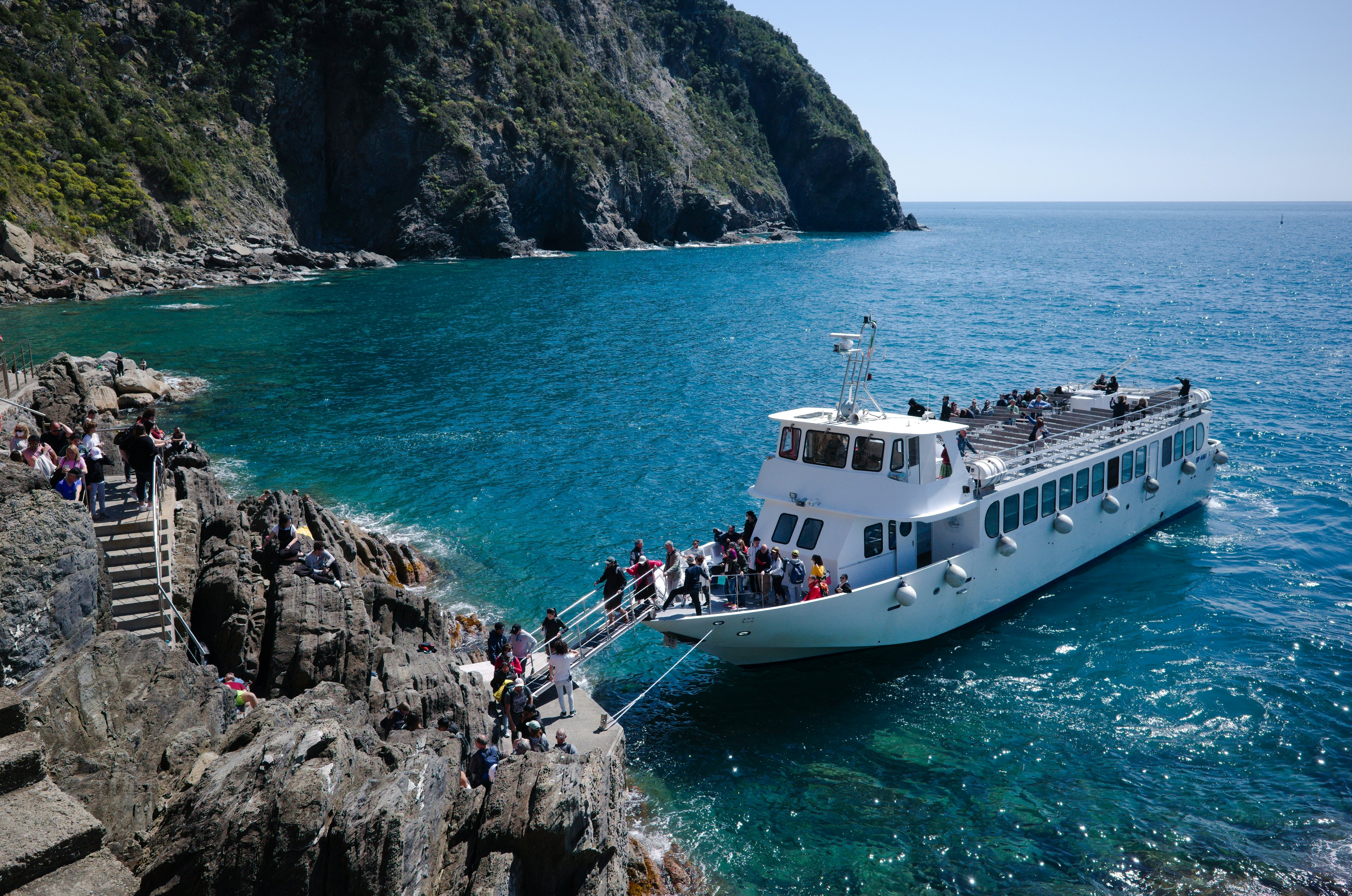 A ferryboat docks at a small pier in a rocky cove in the sea.
