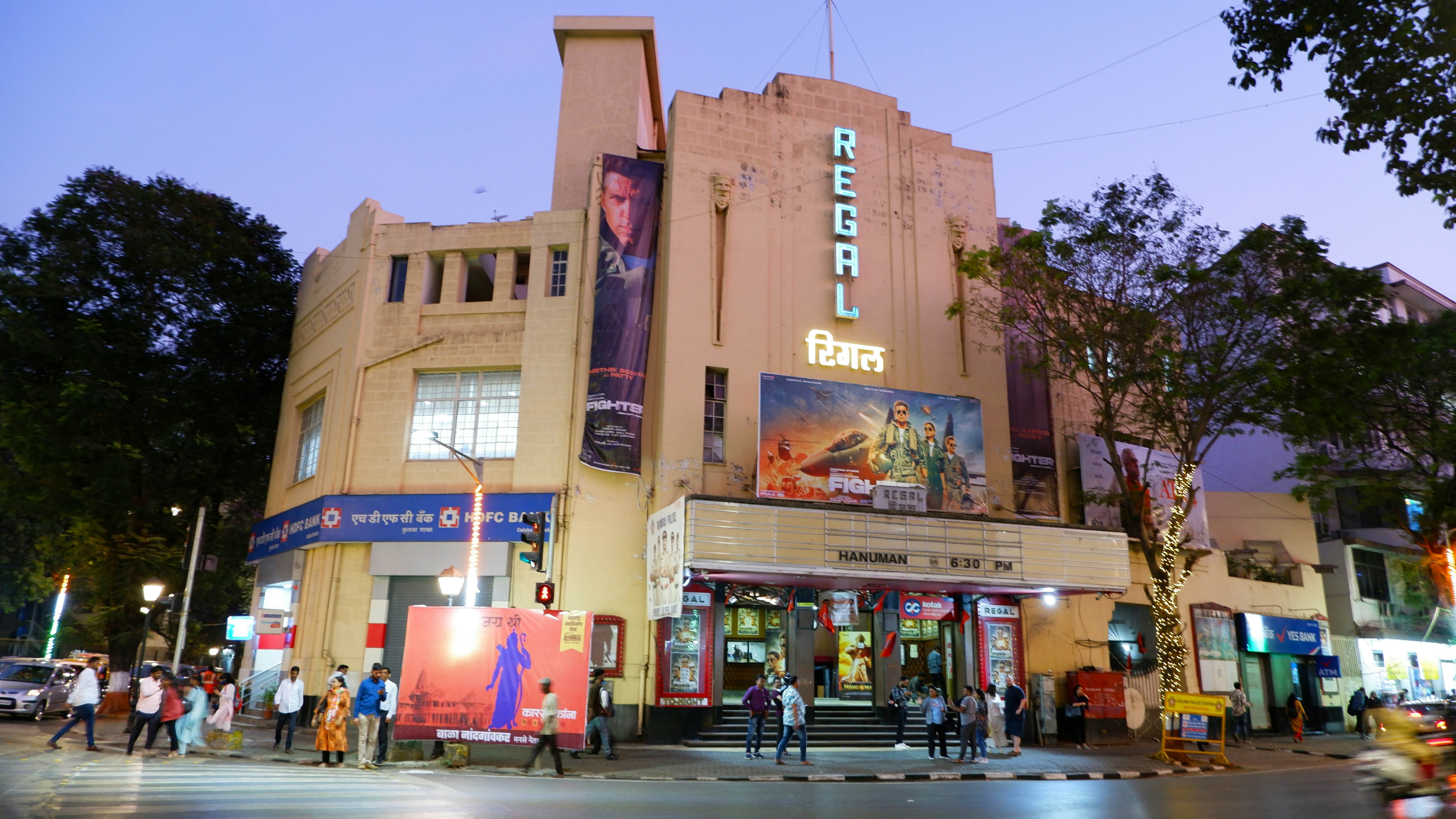 A movie theater in India at night has a vertical sign reading "Regal" lit up and a marquee.