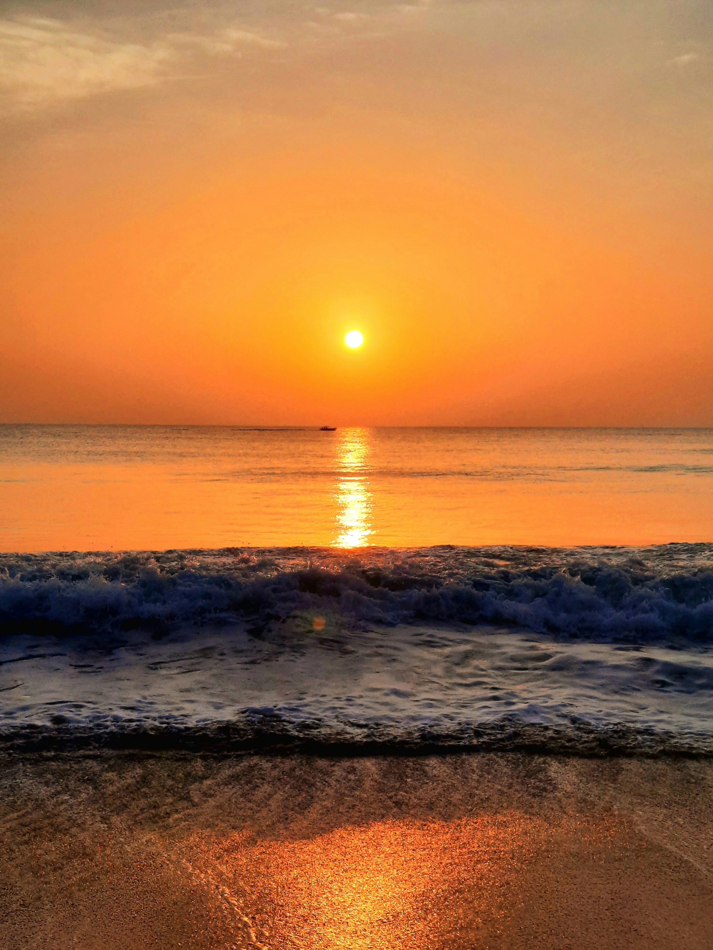 Waves crashing on a beach under a bright orange sky at sunrise