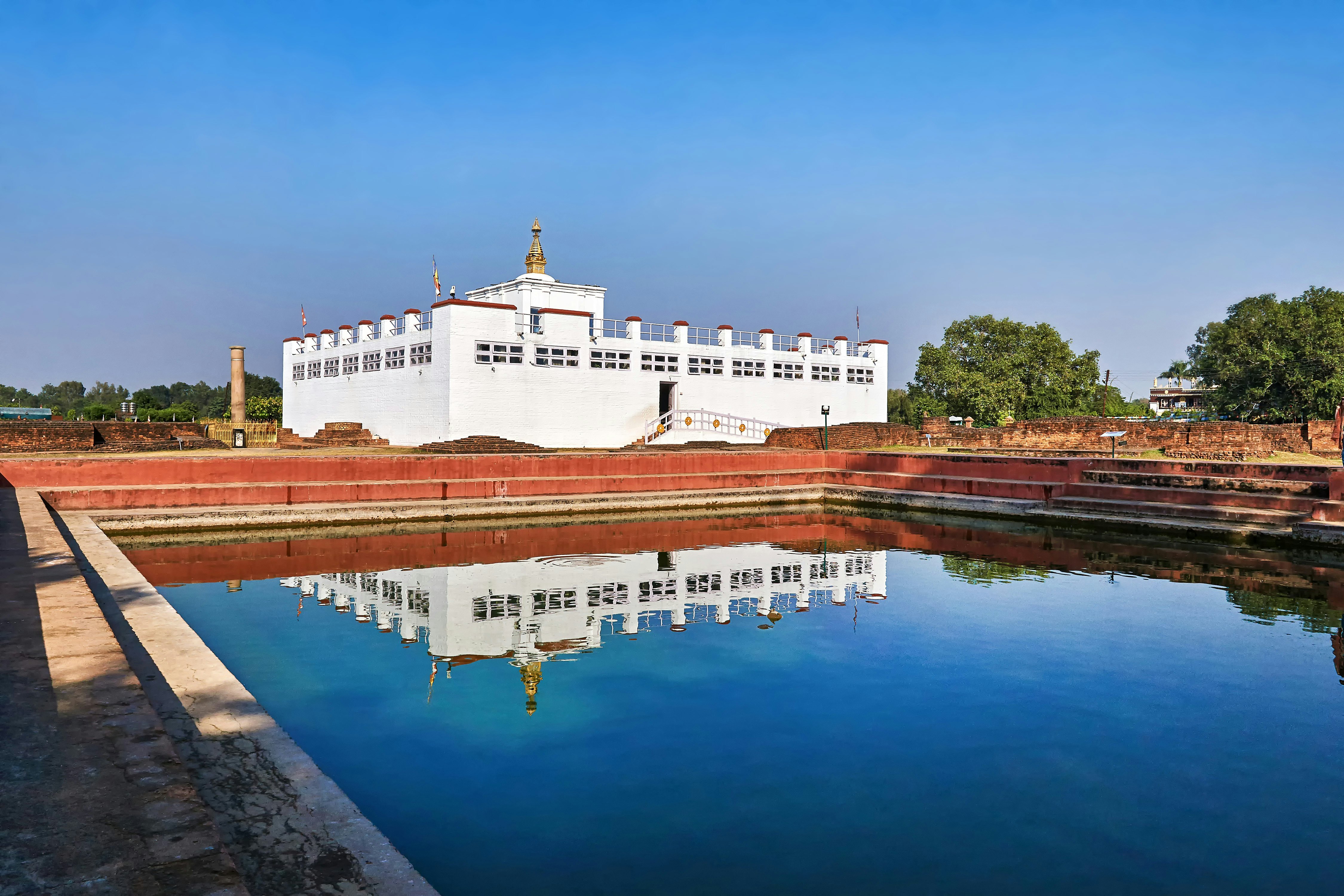 A white rectangular temple building reflected in a nearby pond.