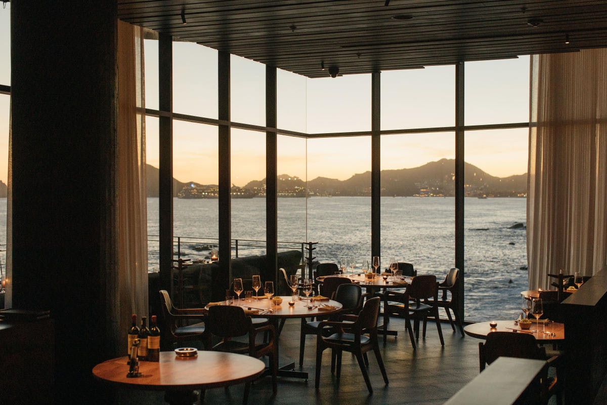 A restaurant with dining tables offers views of the ocean and mountains