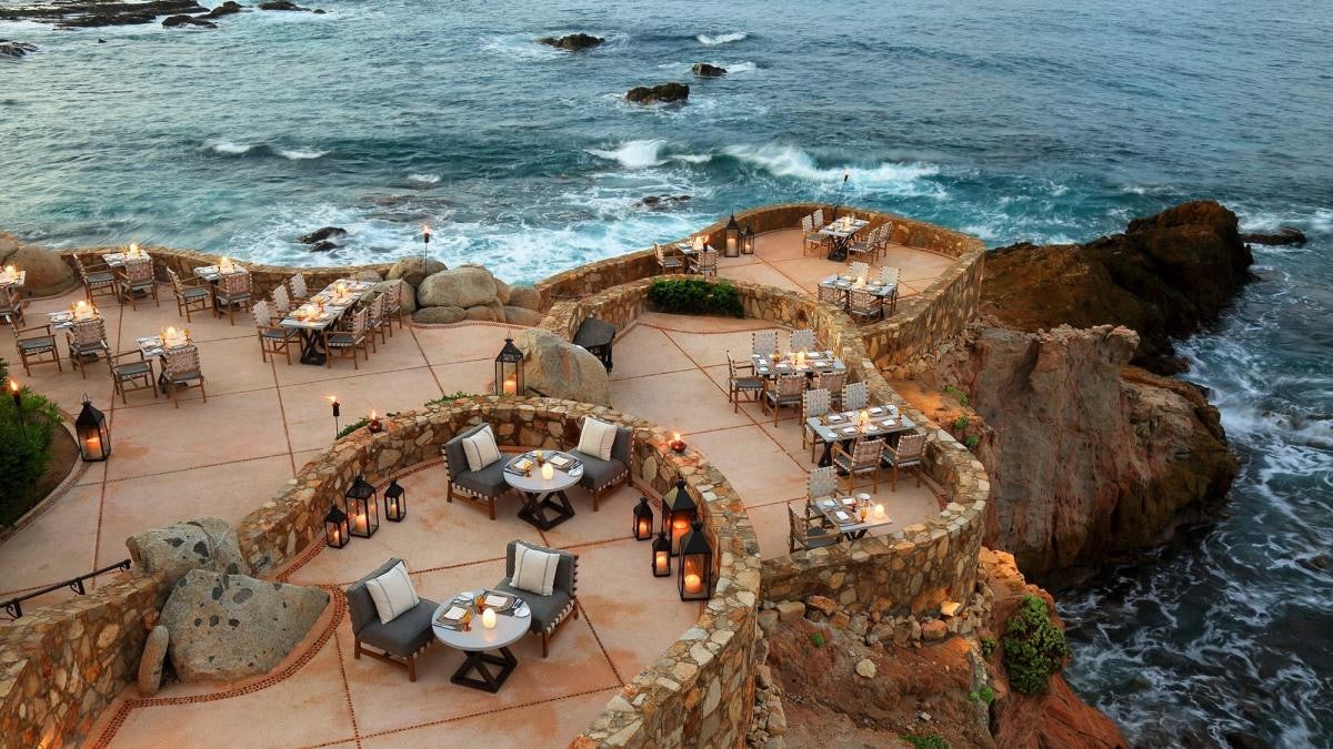 Tables are set up at a cliff restaurant with candles by the sea
