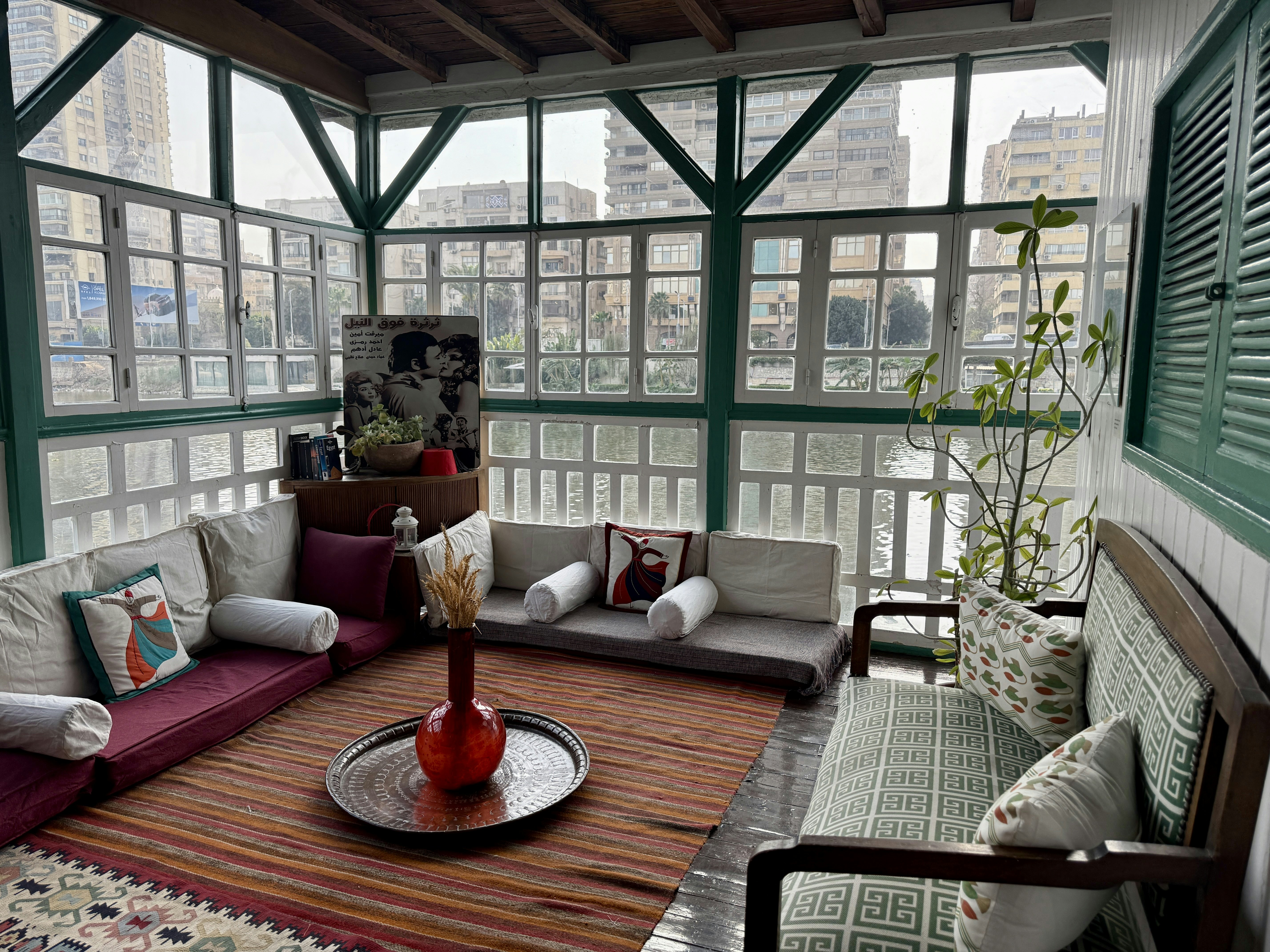 floor sofas with bolster pillows a red stripped rug and surrounded by glass windows overlooking a river