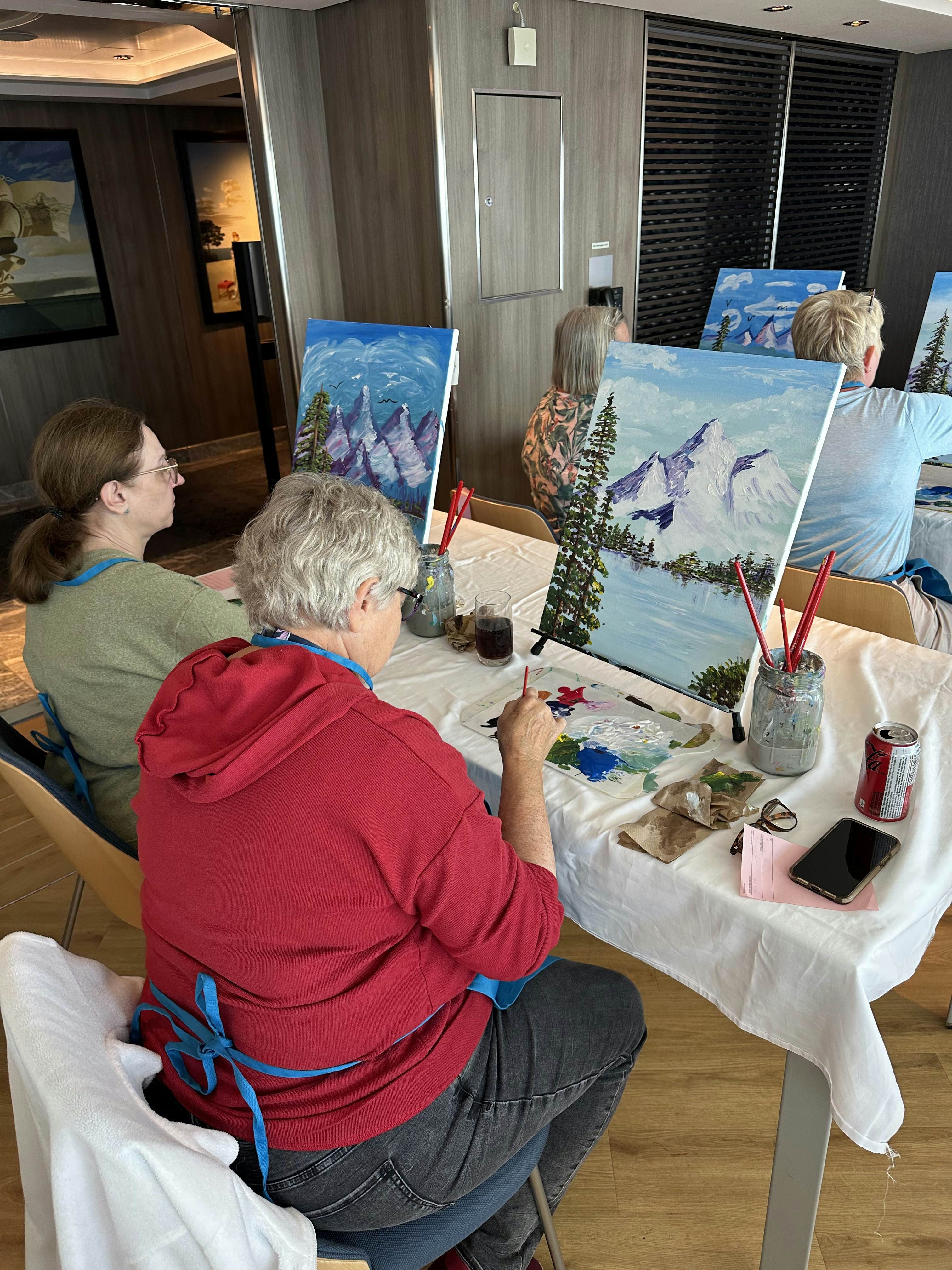 Two people sitting at a table painting on easels.