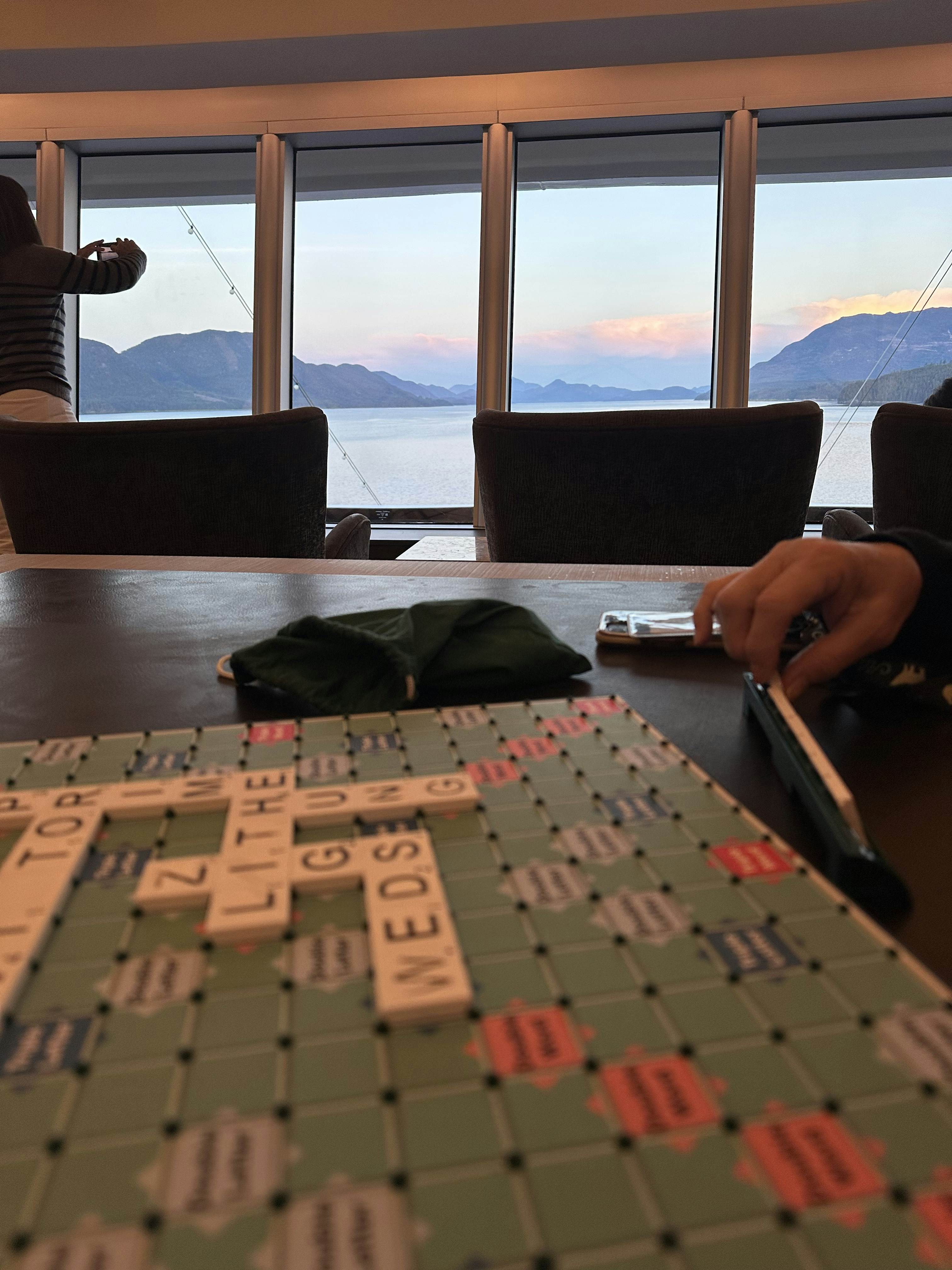 A Scrabble board with a few words on it and the ocean visible through windows in the distance.
