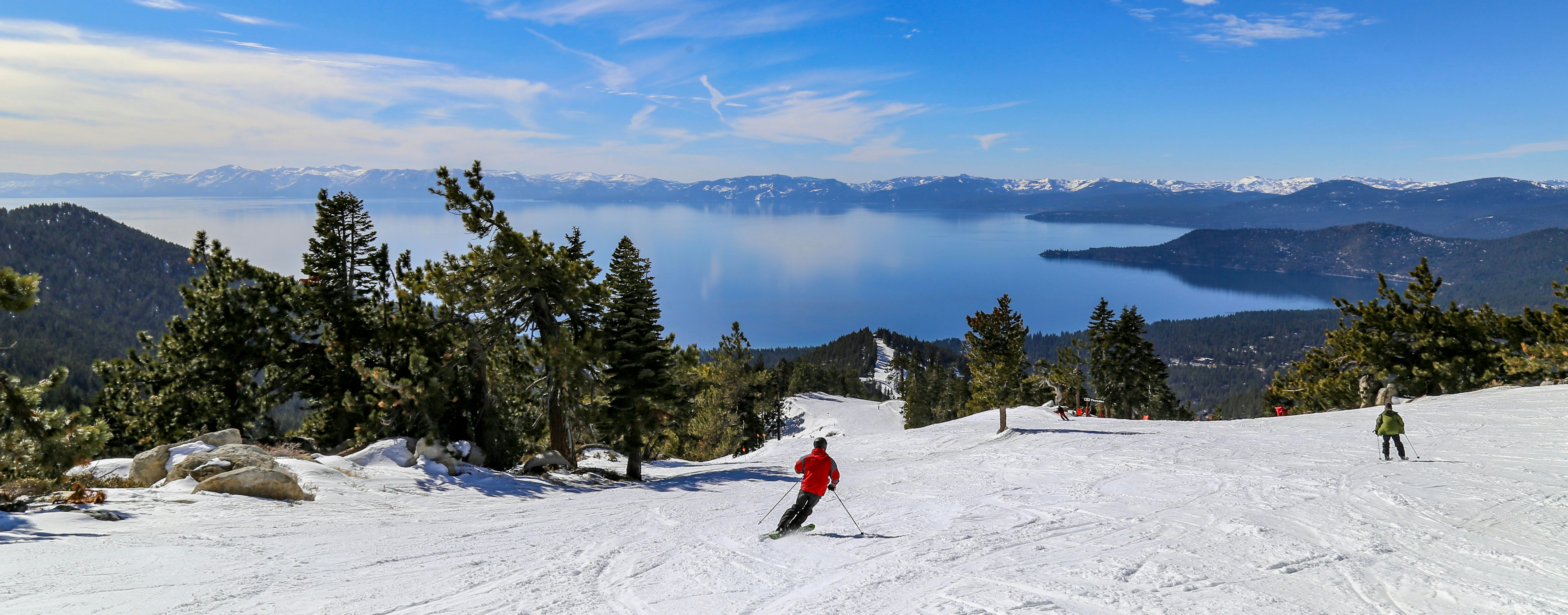 A panorama of a skier in front of a large blue lake on a sunny day.