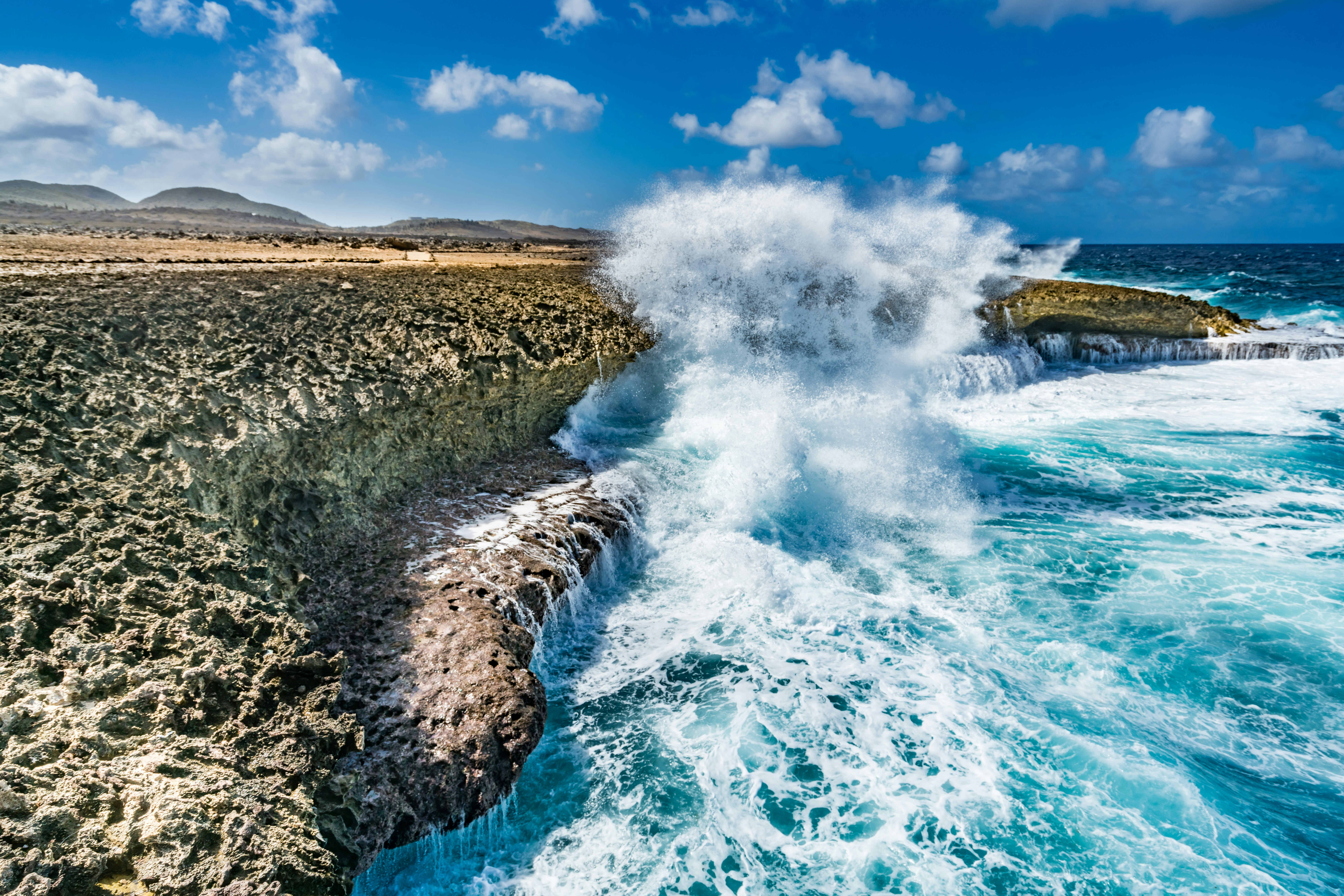 Waves crash against rocky cliffs, throwing off white surf.