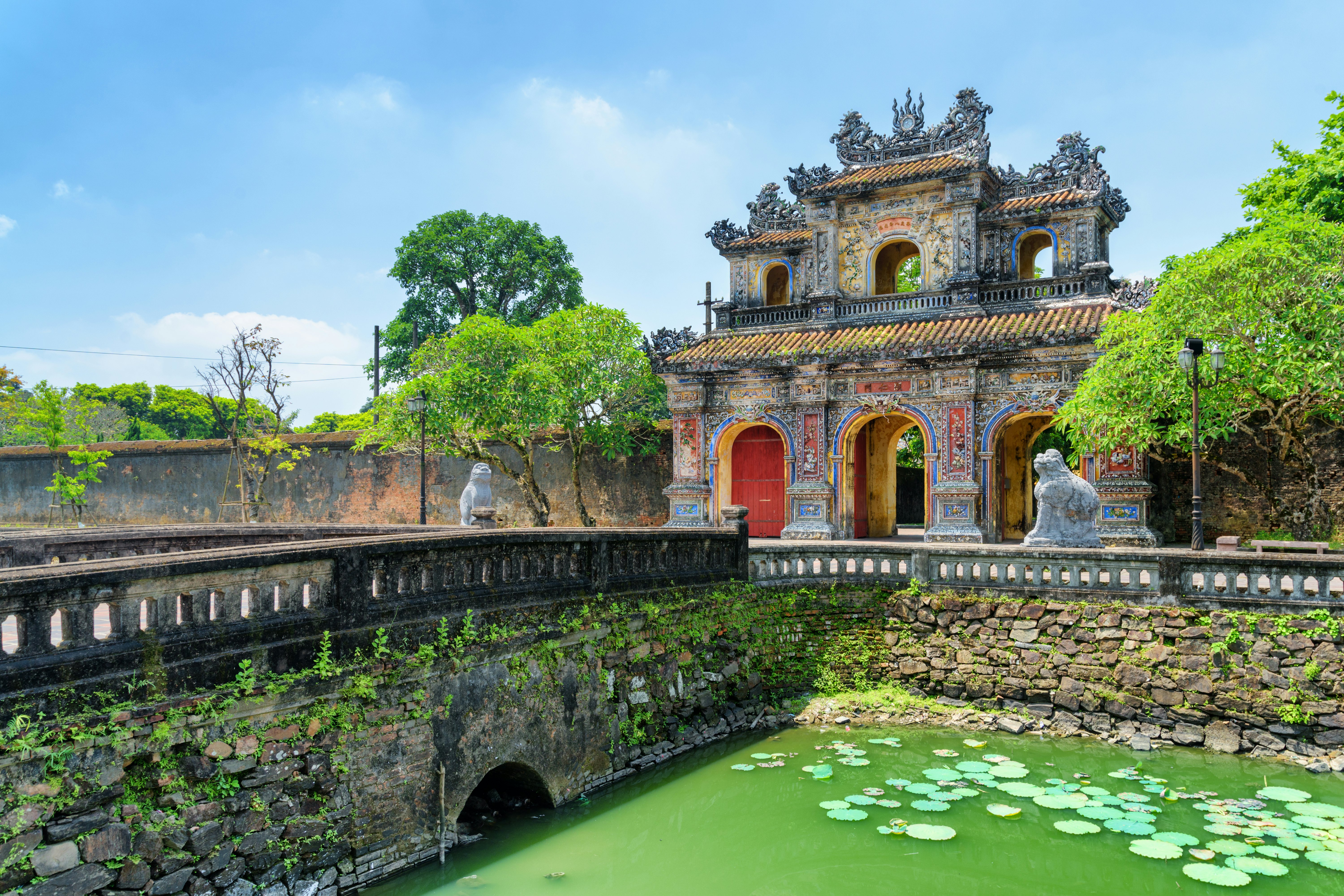 An ornate gateway to an ancient walled city beside a river with green lily pads.