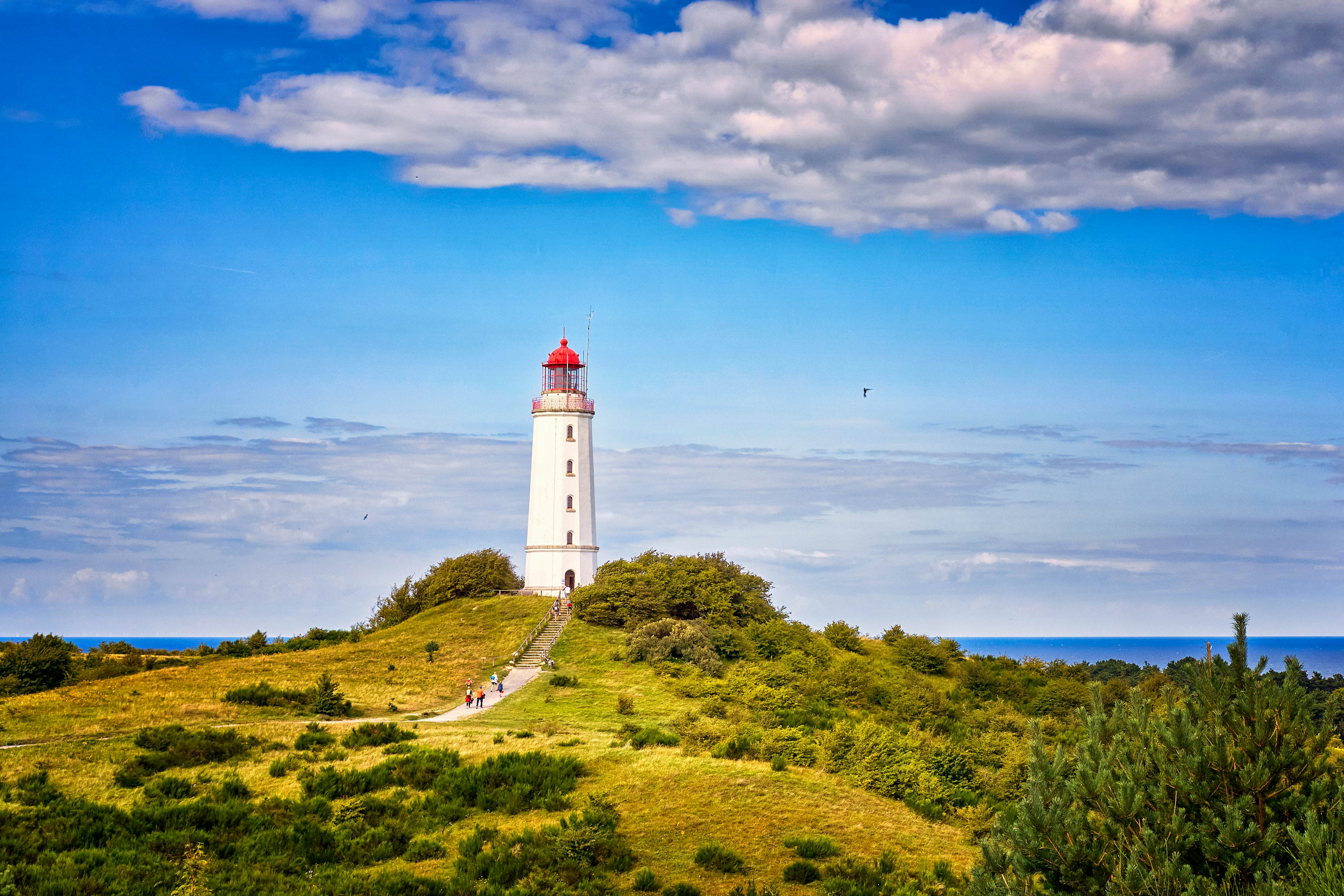 A lighthouse on a grassy hill overlooking a waterway on a bright, sunny day.