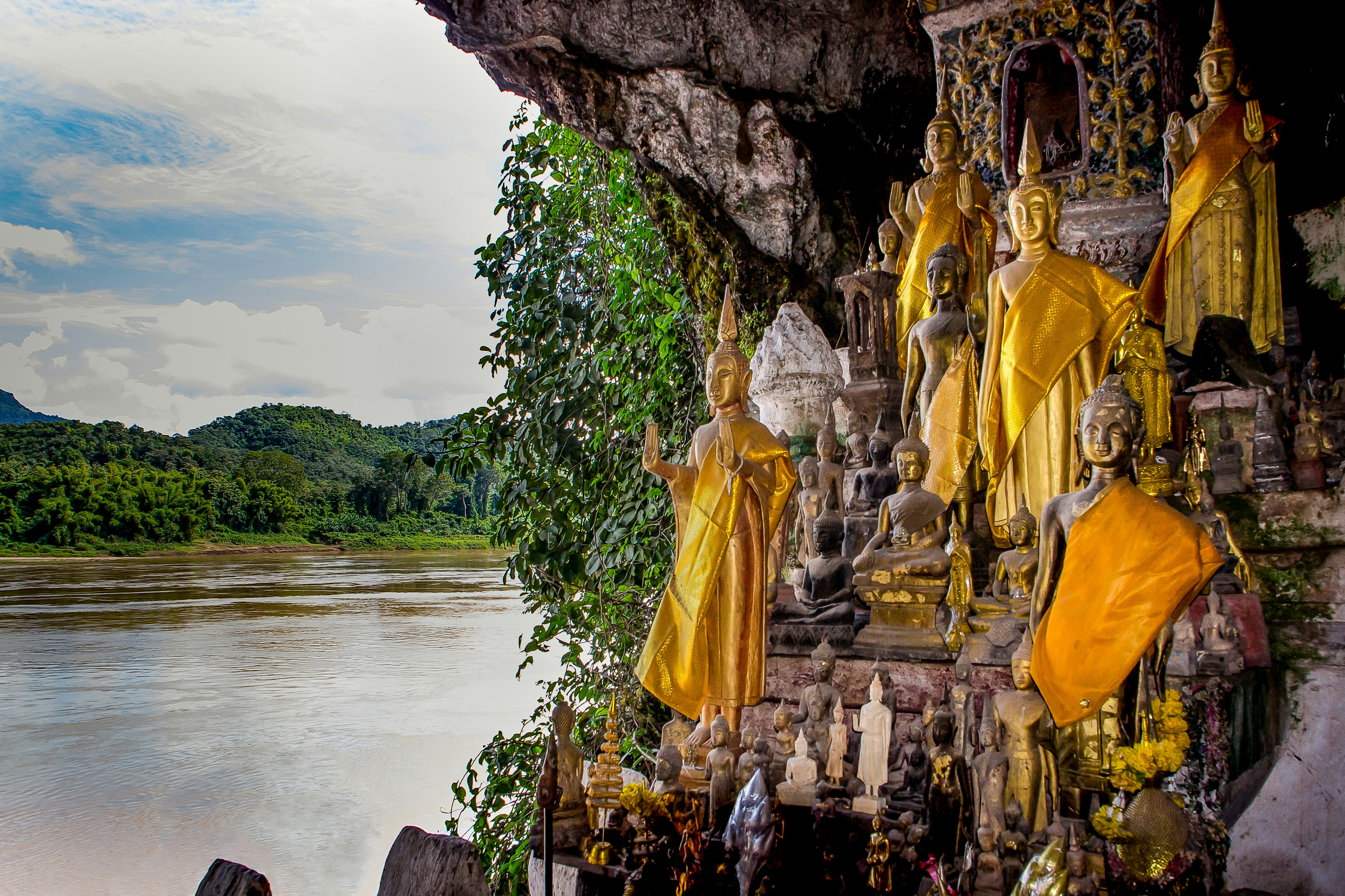 A series of Buddha statues stand inside a riverside cave.