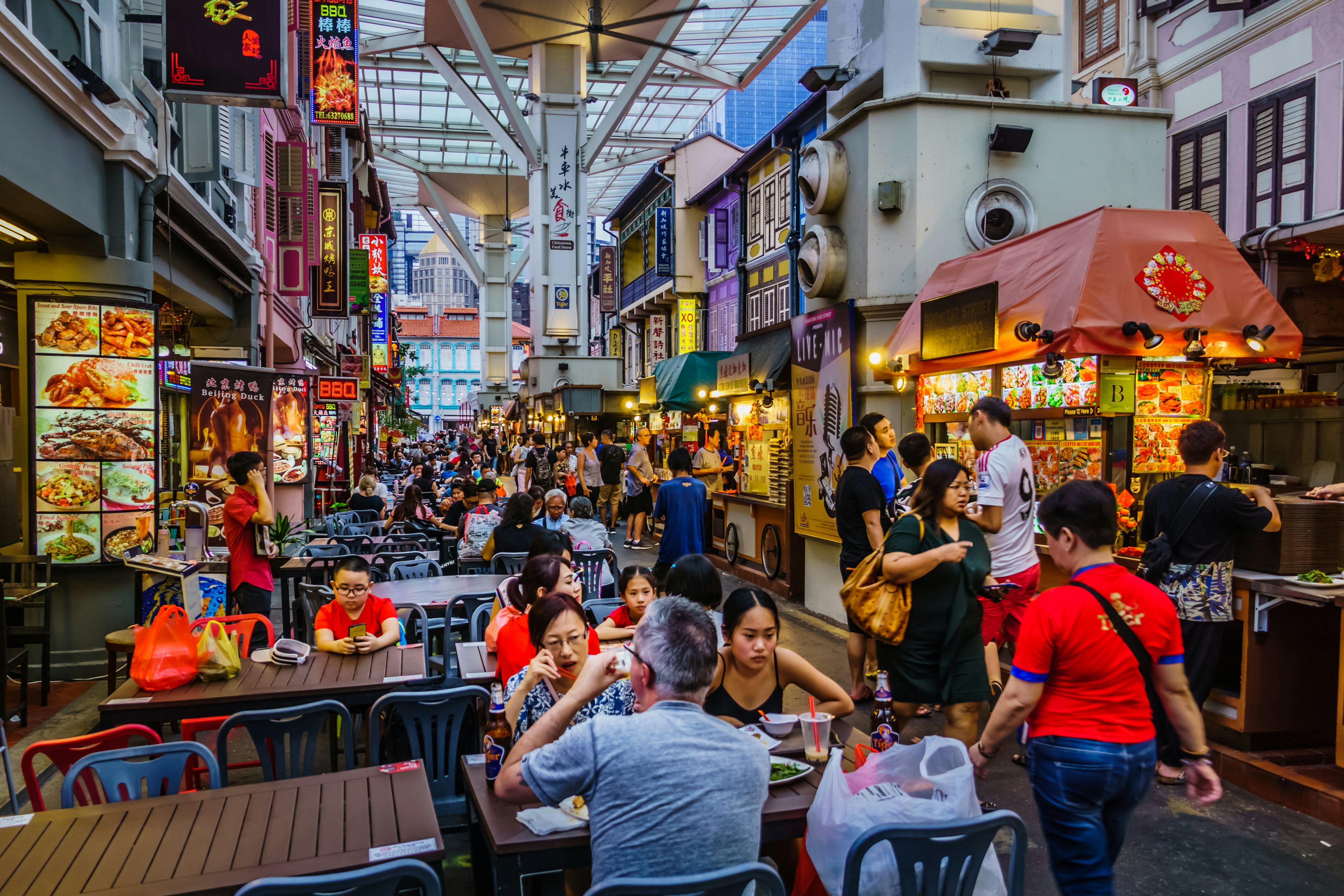 People walk by tables and food stalls in a covered food court.