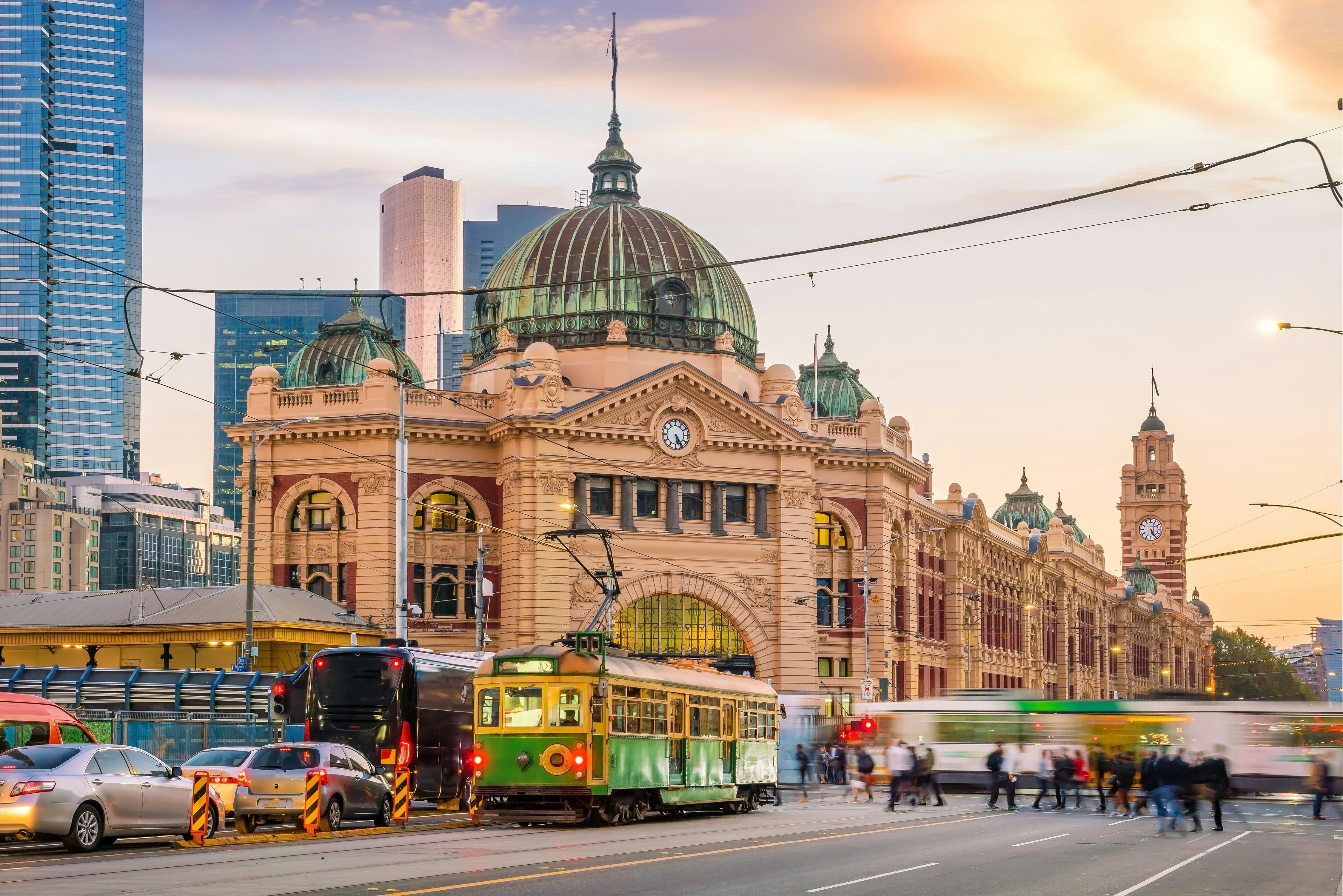 Trams pass in front of Melbourne's Flinders Street Station in Australia at sunset.