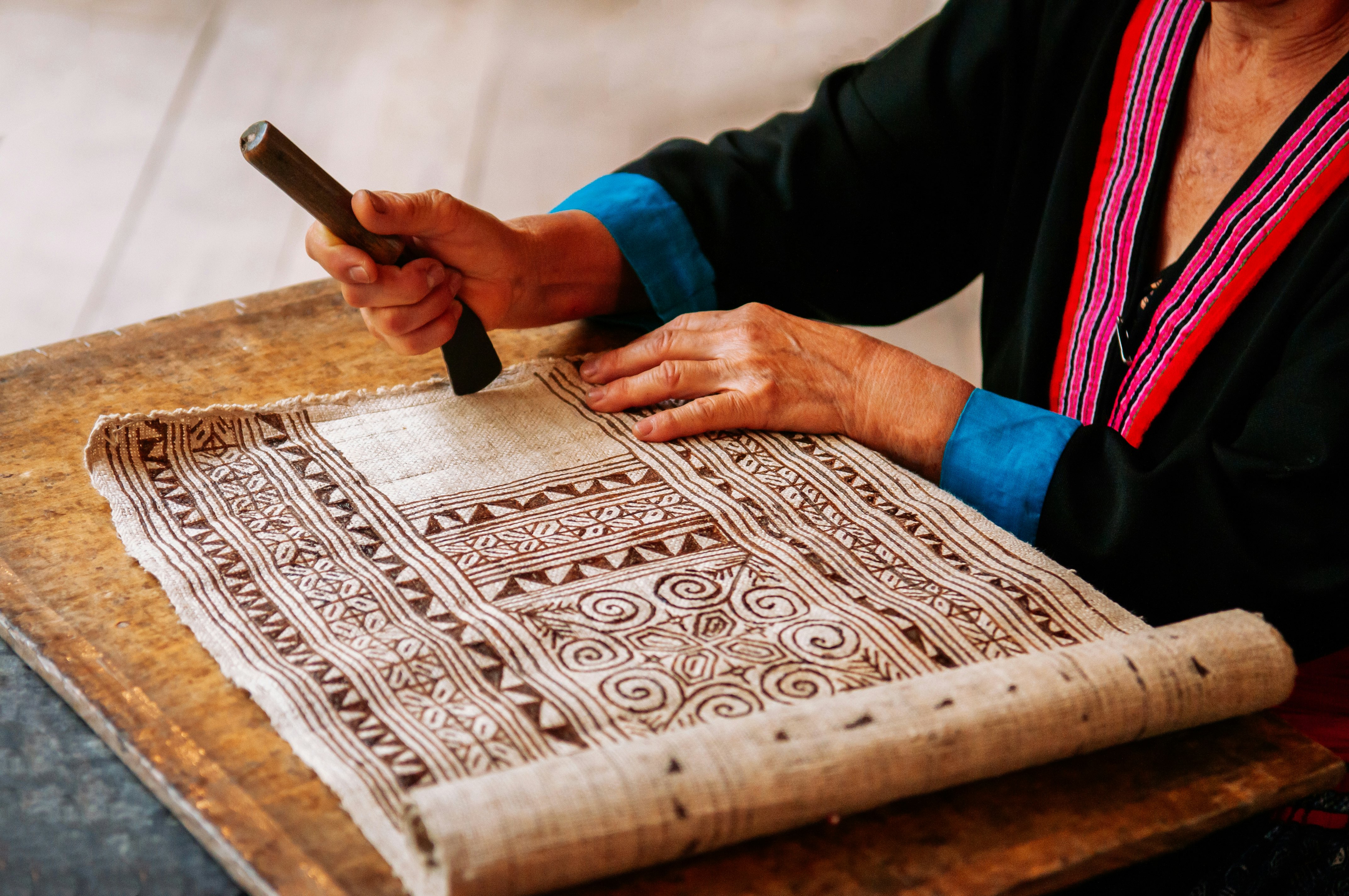 A person works on a batik textile with a geometric design.